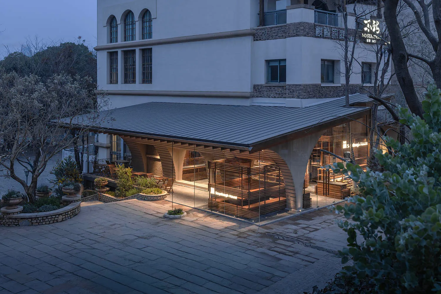 一棟石頭建築搭配木質屋頂和大型窗戶，自然光線照射下，營造出溫暖與邀人的氛圍