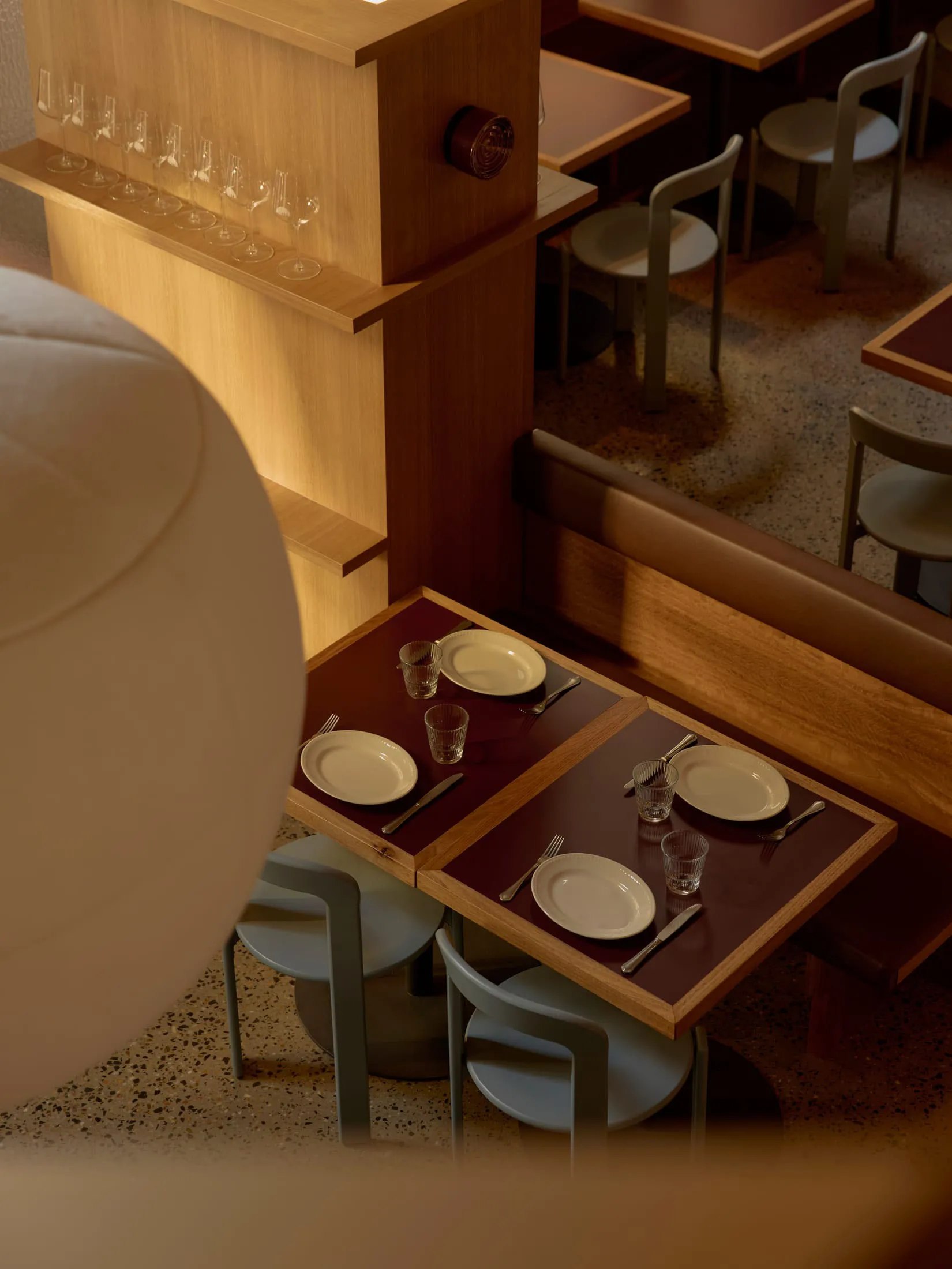 A dimly lit restaurant with wooden floor and tables set with plates, silverware, and glasses, featuring a modern style with wood and metal elements