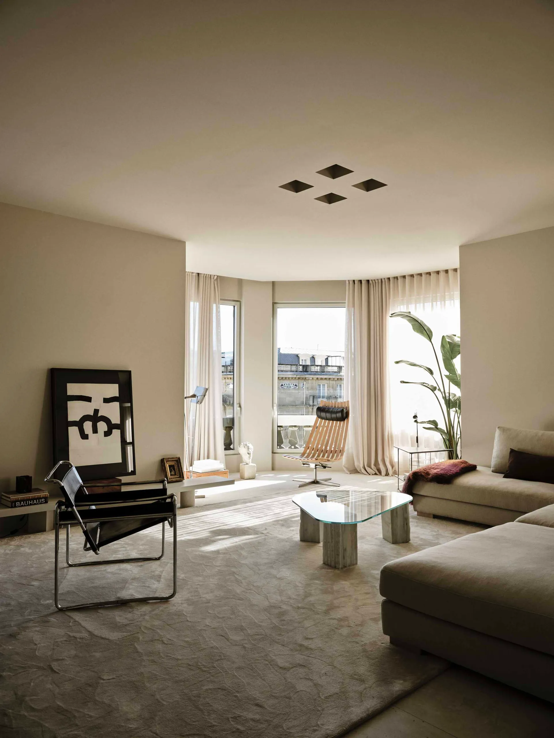 A well-lit living room with a couch, chair, and glass table, furnished with a potted plant, vase, and book, creating a modern and inviting space for relaxation and socializing