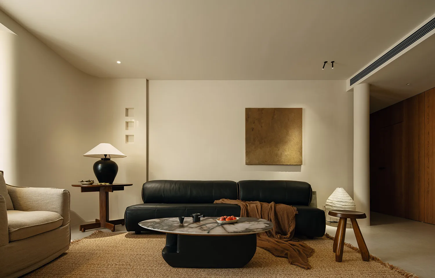 A modern living room with a black couch, coffee table, and lamp, featuring a clean and minimalist design and well-lit atmosphere