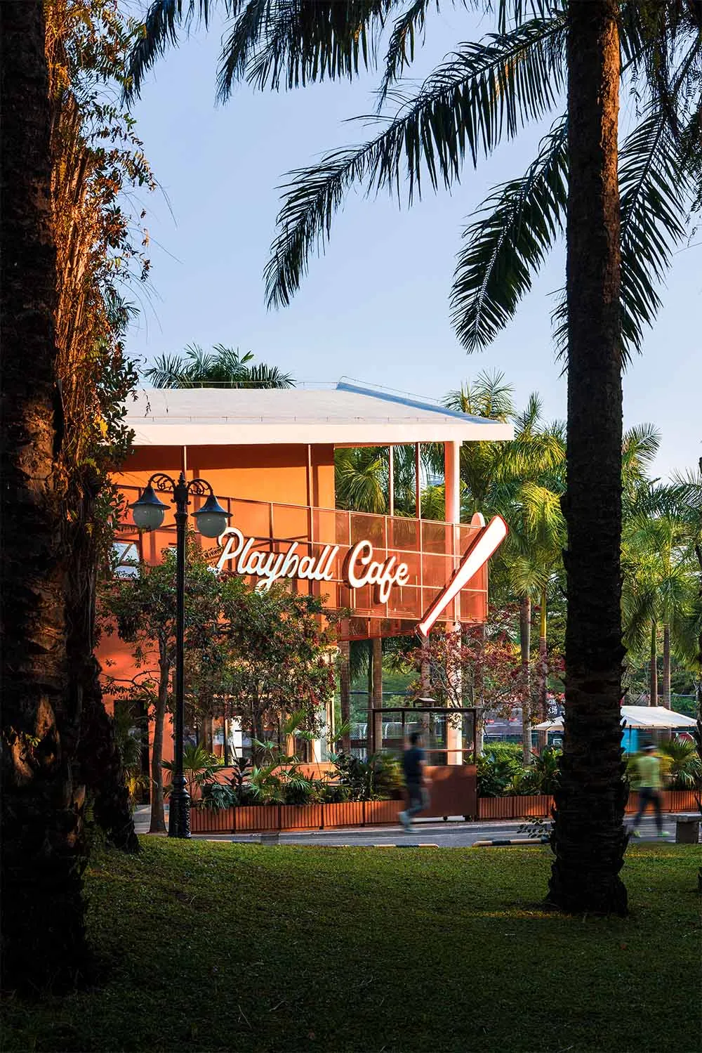 A modern restaurant with a wooden exterior, palm tree, and natural lighting, filled with furniture and people enjoying the outdoor ambiance