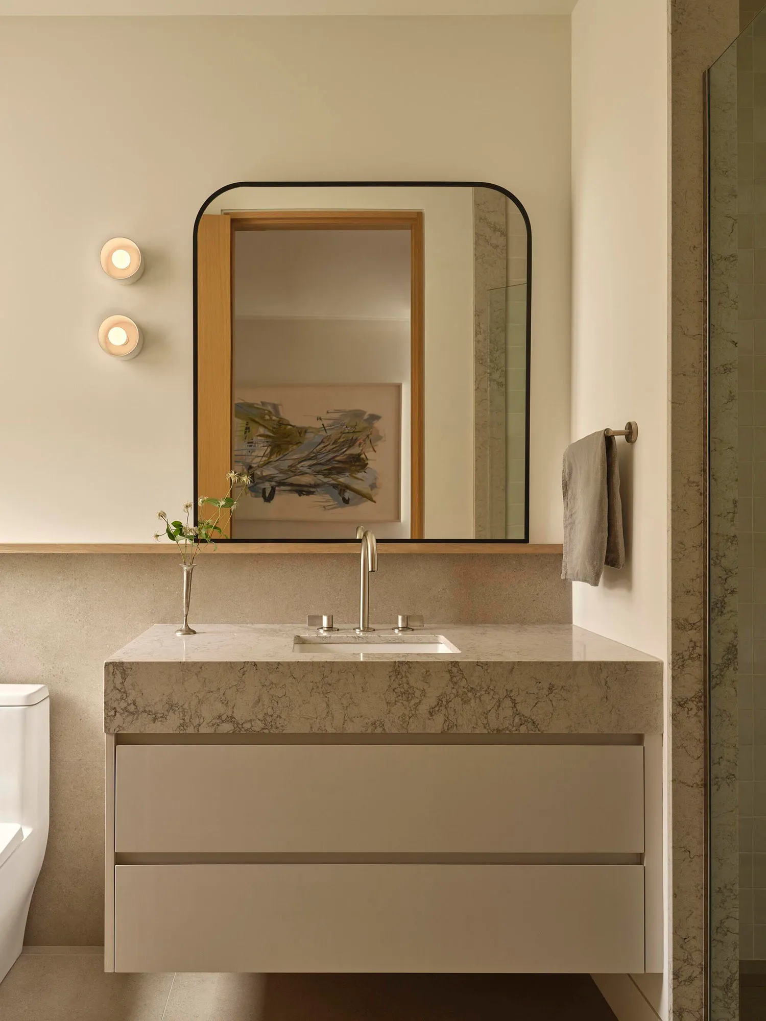 Bathroom with a white color scheme, dim lighting, and a marble sink, mirror, and towel rack