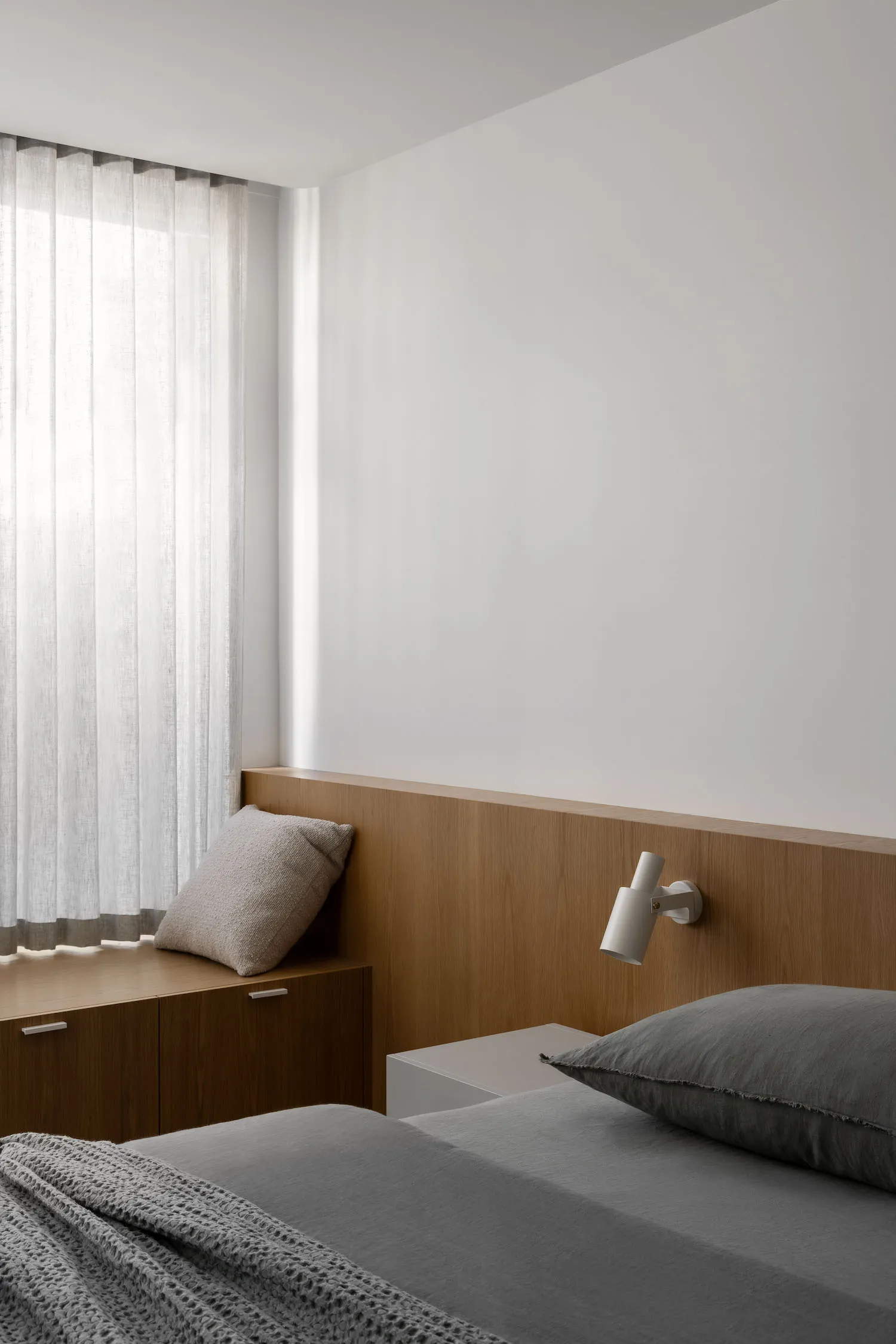 Cozy bedroom with a wooden bench, white walls, and a window with curtains, lit by a lamp