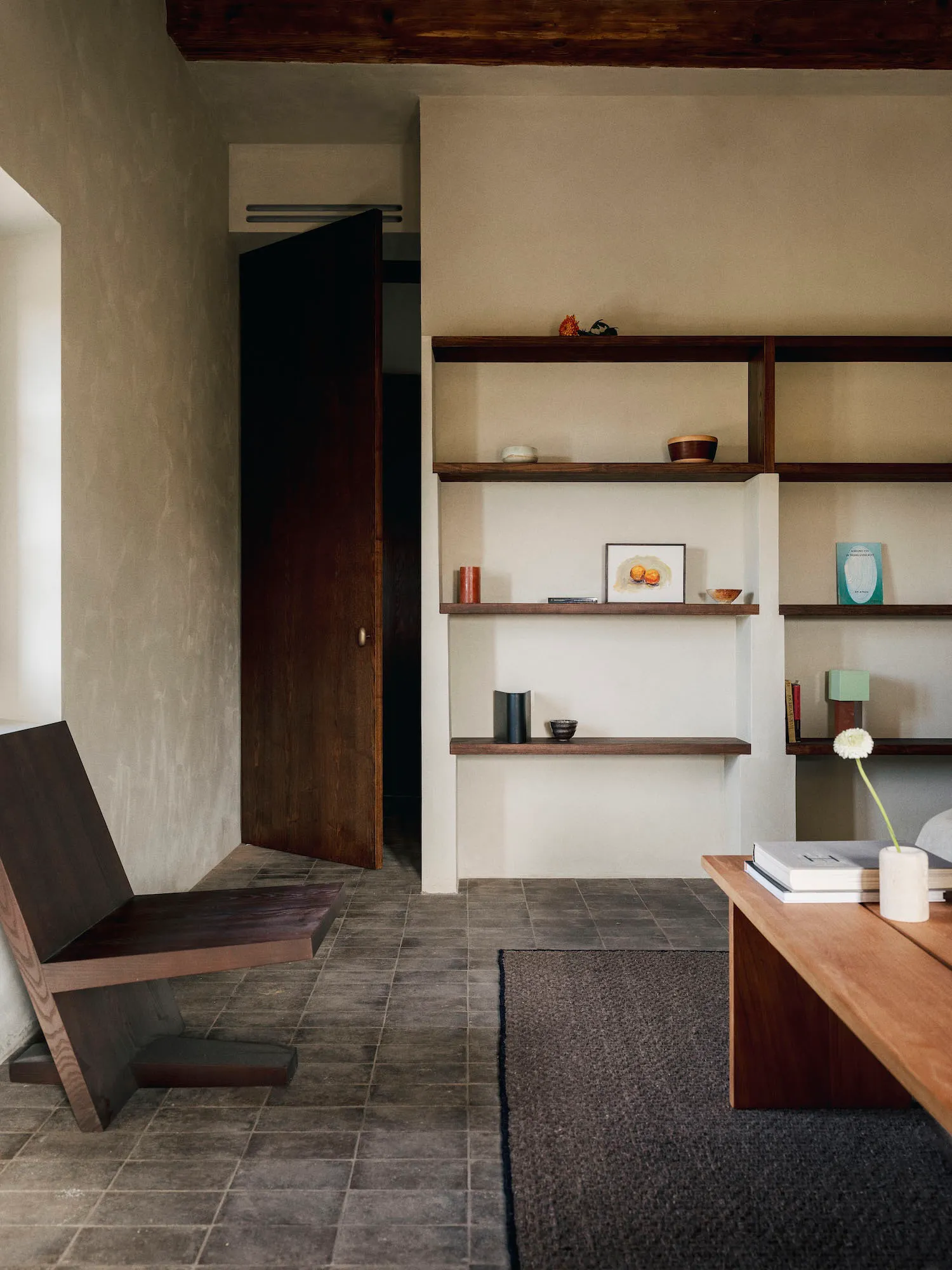 A well-lit living room with a wooden floor, a bookshelf, a chair, a table, and a vase, creating a warm and inviting atmosphere