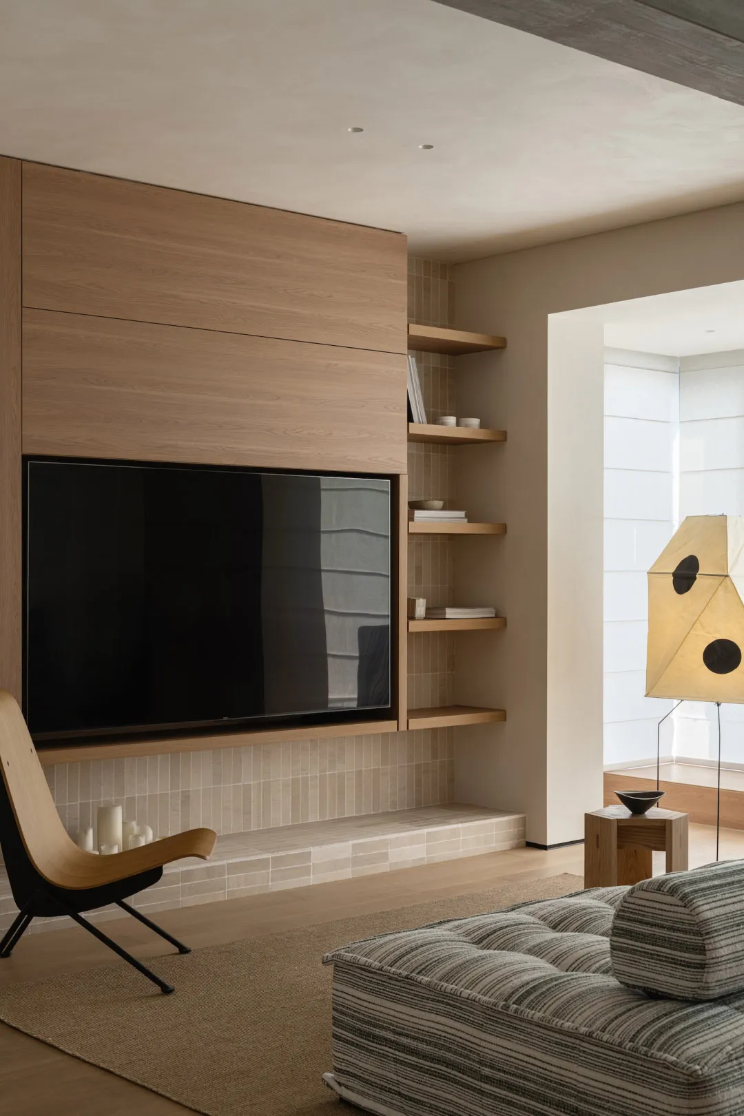 Comfortable living space with a couch, chair, and bookshelf, featuring a mix of natural and artificial lighting, wood, and glass materials
