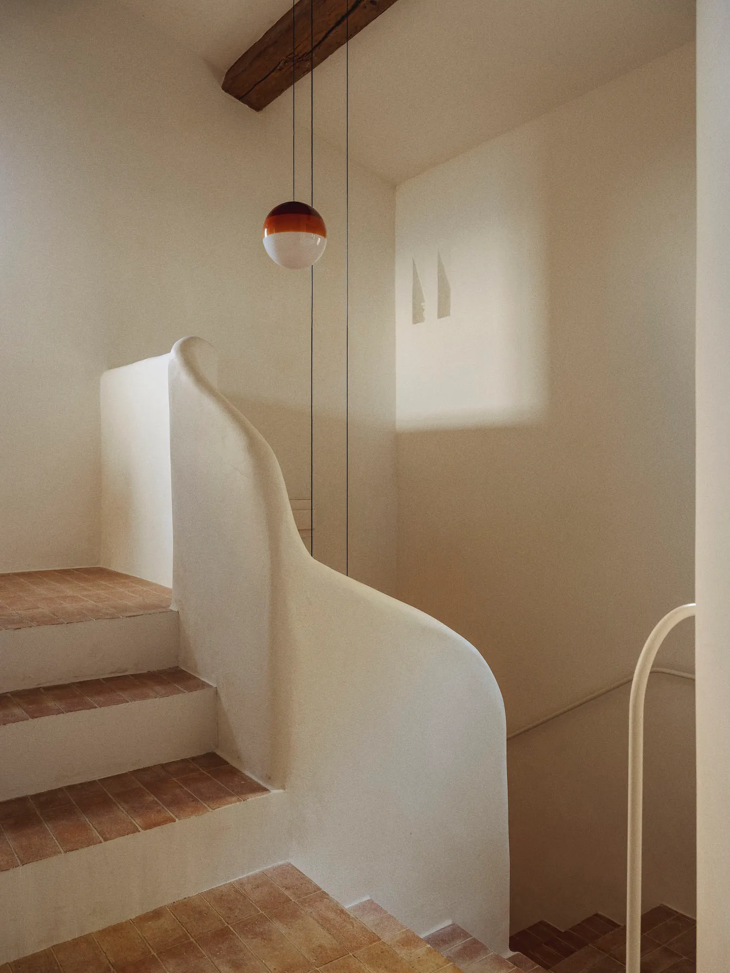 A modern staircase with a white wall and concrete floor, surrounded by a minimalist atmosphere with natural light
