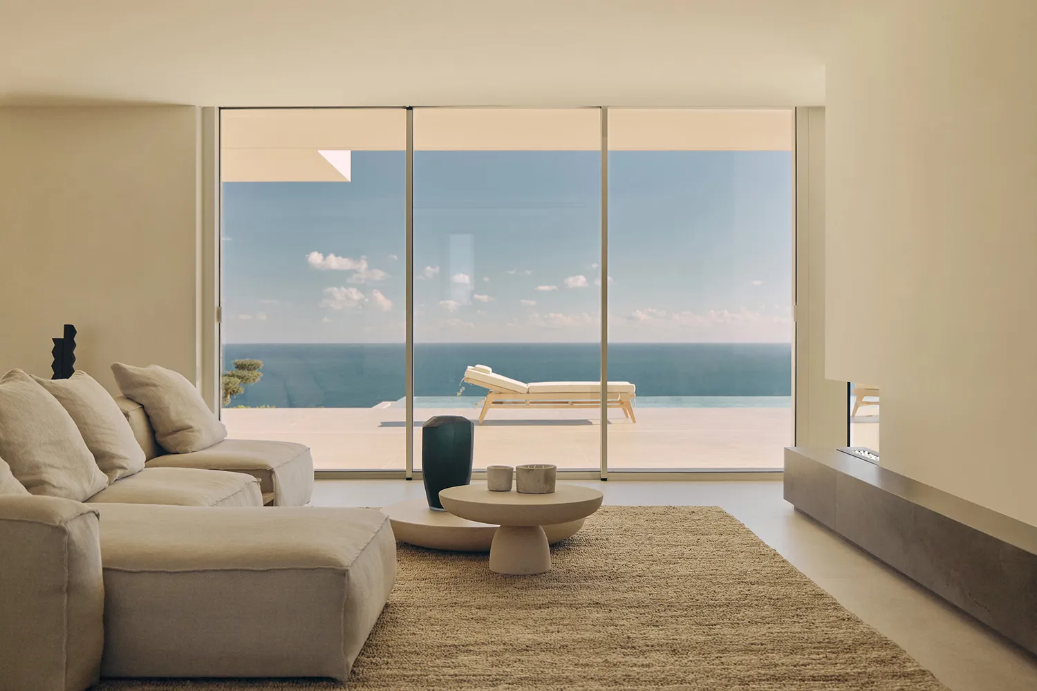 Coastal living room with a modern sofa, armchair, coffee table, and decorative items, set against a large window with an ocean view