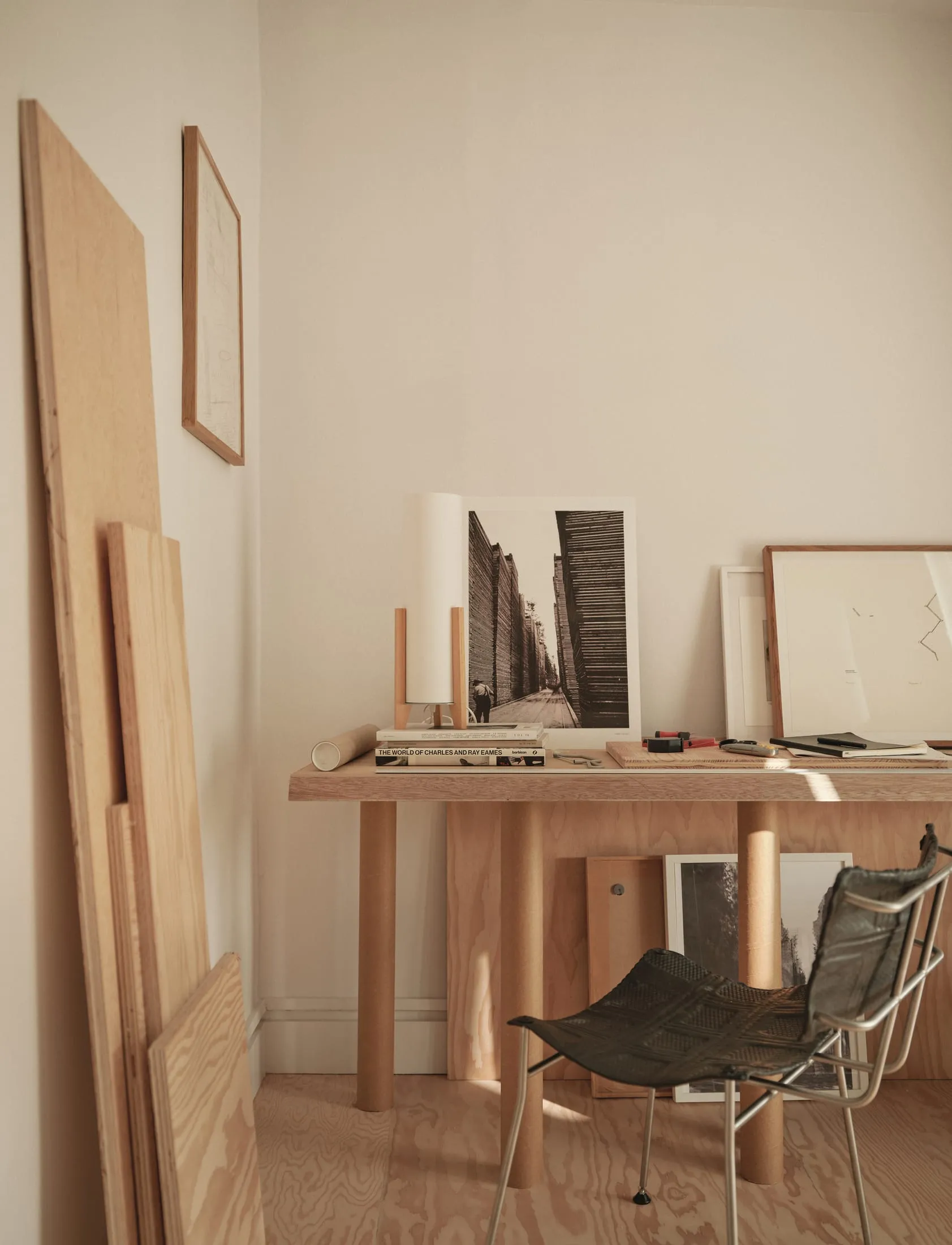 A cozy home office with a wooden desk, chair, and various items, including a book, cup, and vase, in a living space with a focus on the desk area
