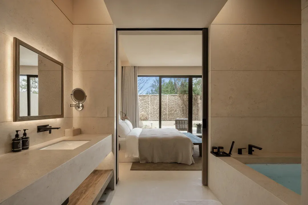 A modern minimalist bedroom with a bed, sink, and door, featuring predominantly white surfaces and a clean appearance
