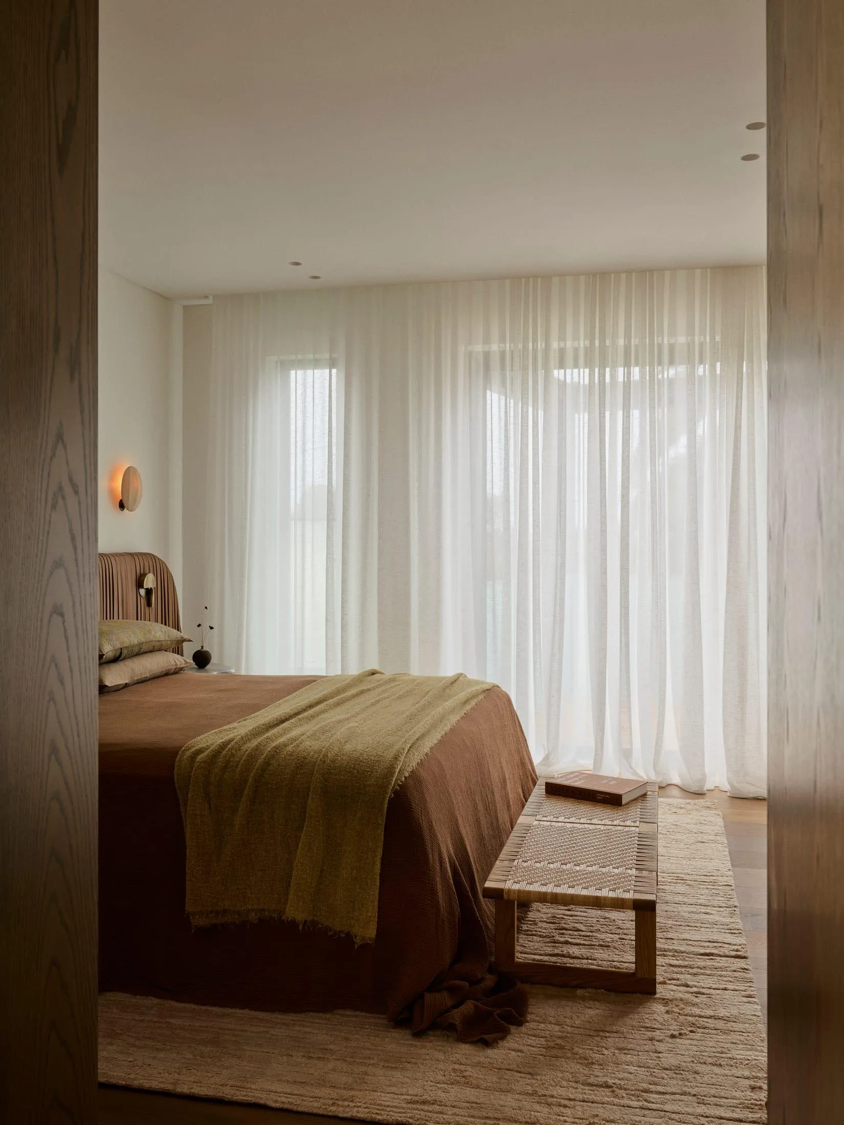 Cozy bedroom with a brown-covered bed, a bench, and natural light from a window