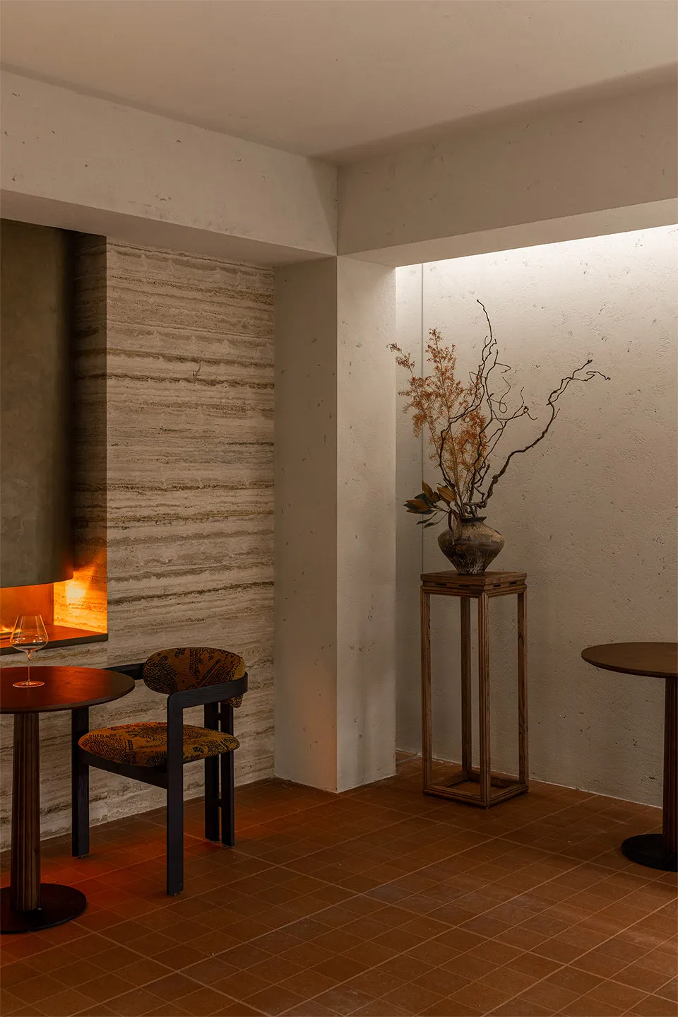 A warm and inviting dining area with a wooden table, chairs, and a vase with flowers, surrounded by stone walls and soft warm lighting