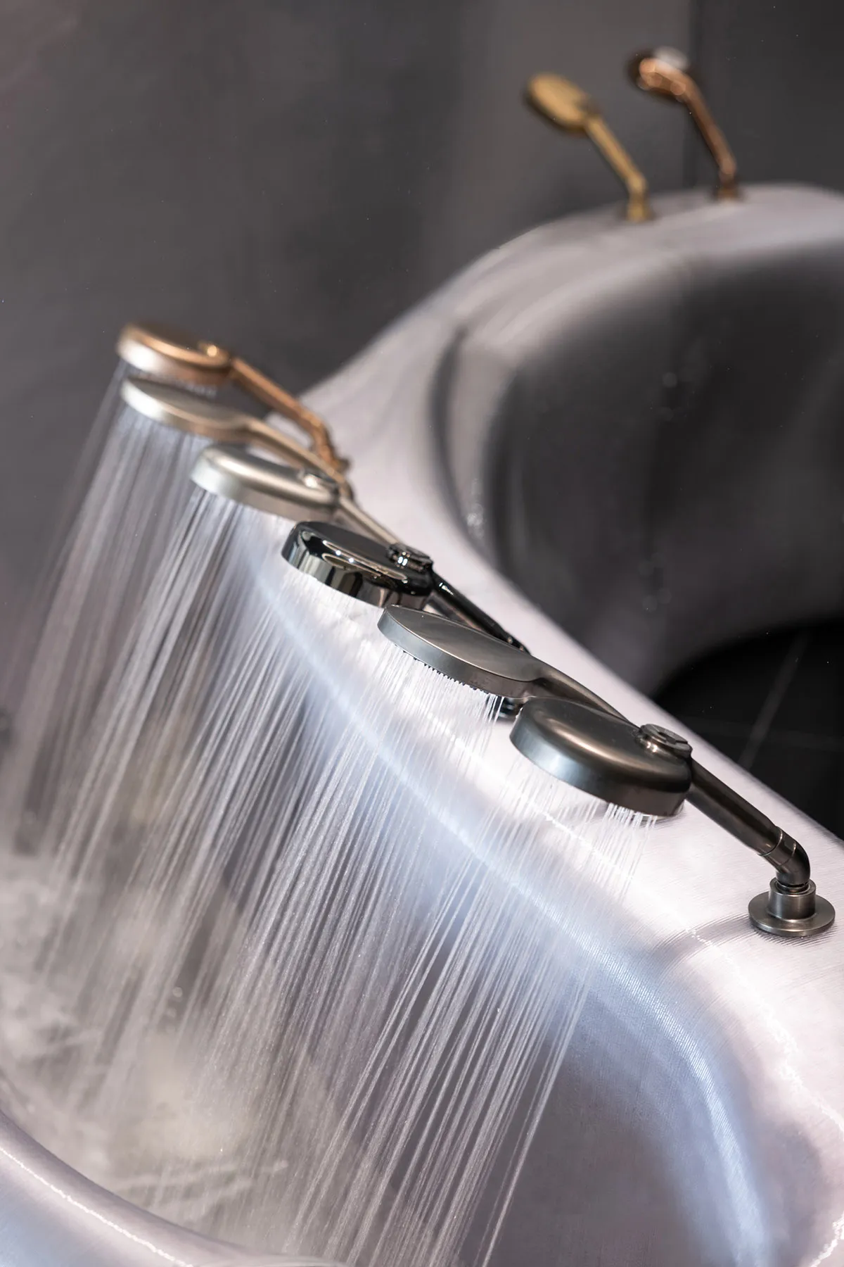 A modern bathroom with a metal sink and brass shower head, featuring dim lighting and a moody atmosphere