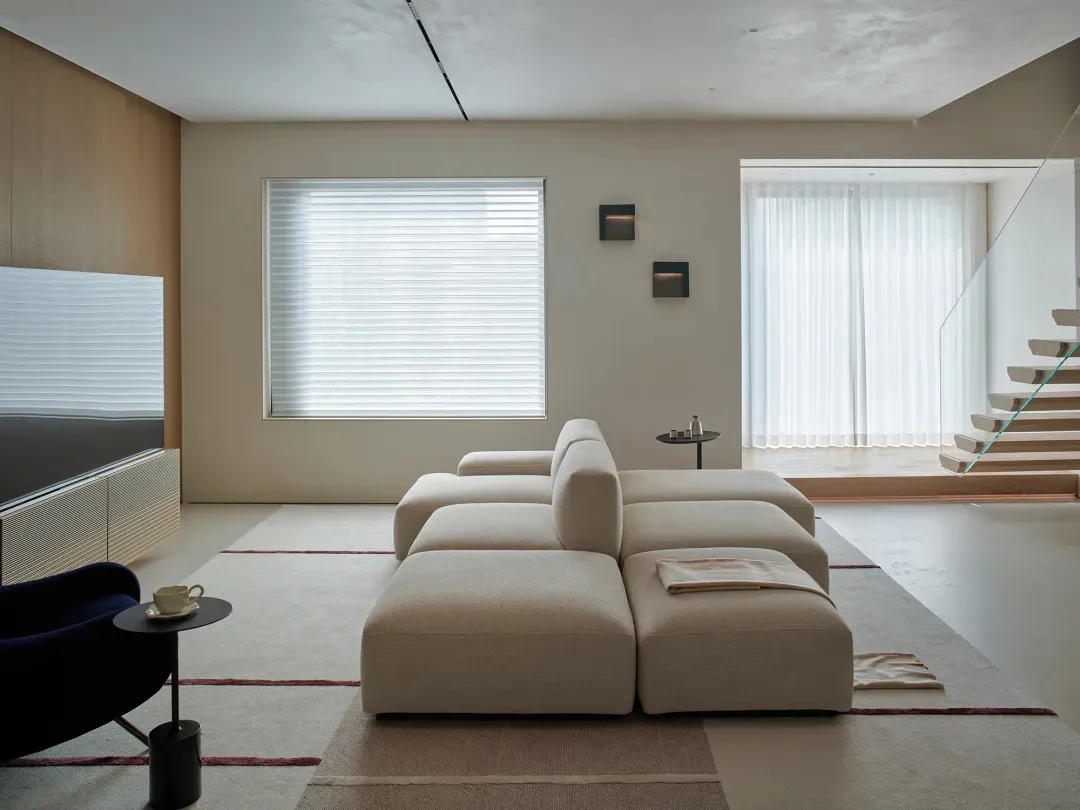 A modern living room with a white couch and chair, a TV on the left, and a coffee table in the center, set in a well-lit space with a clean design