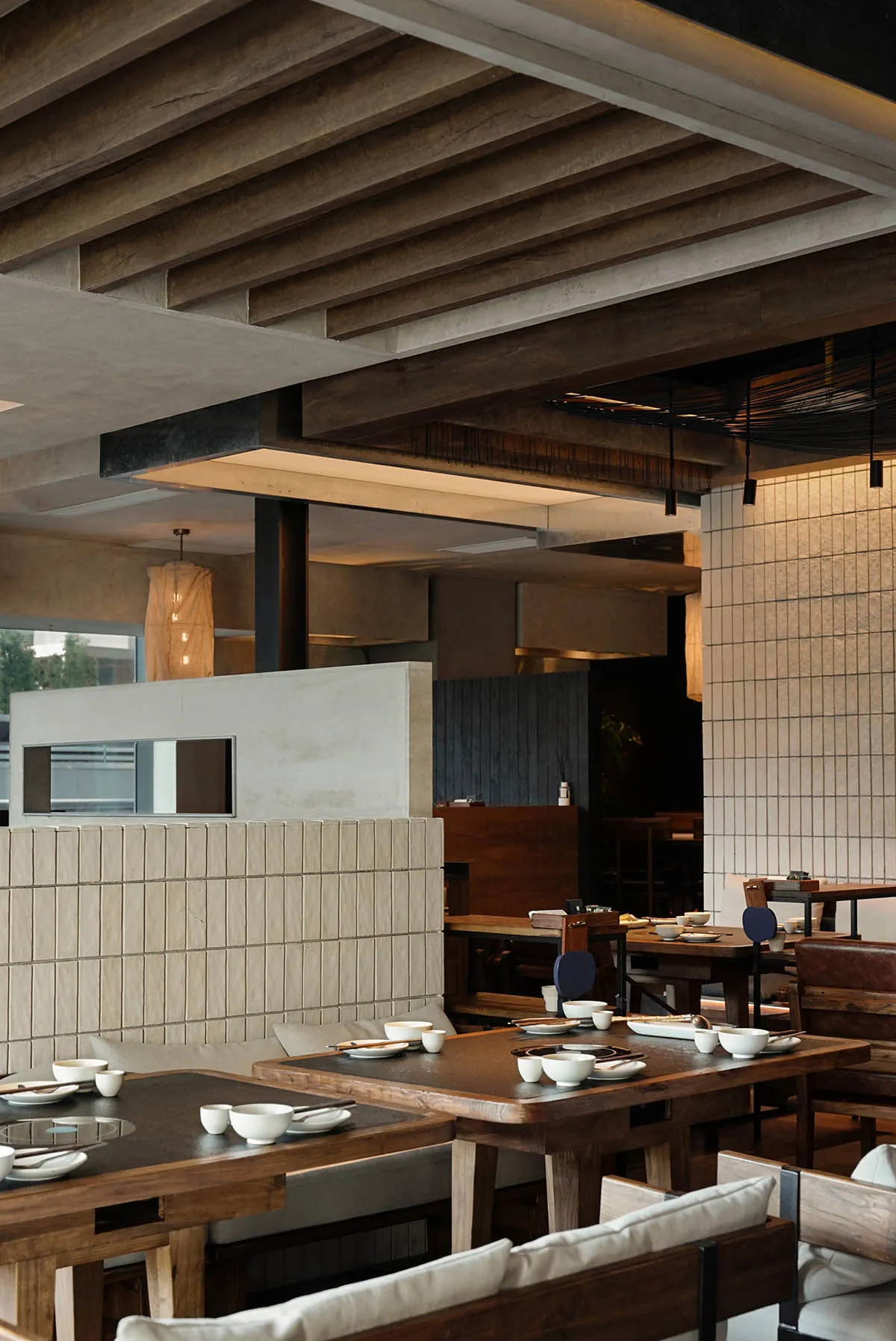A modern restaurant interior with wood paneling, natural lighting, and a variety of materials, featuring tables, chairs, and dining area