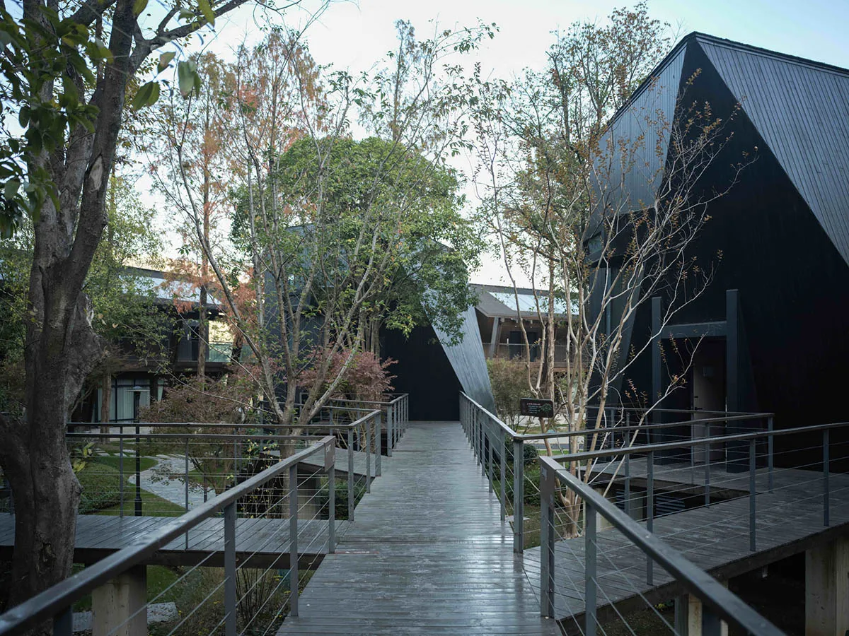 一座現代黑色家園，配有木質步道和金屬欄杆，環繞著樹木，充滿自然光線和明亮的氣氛
