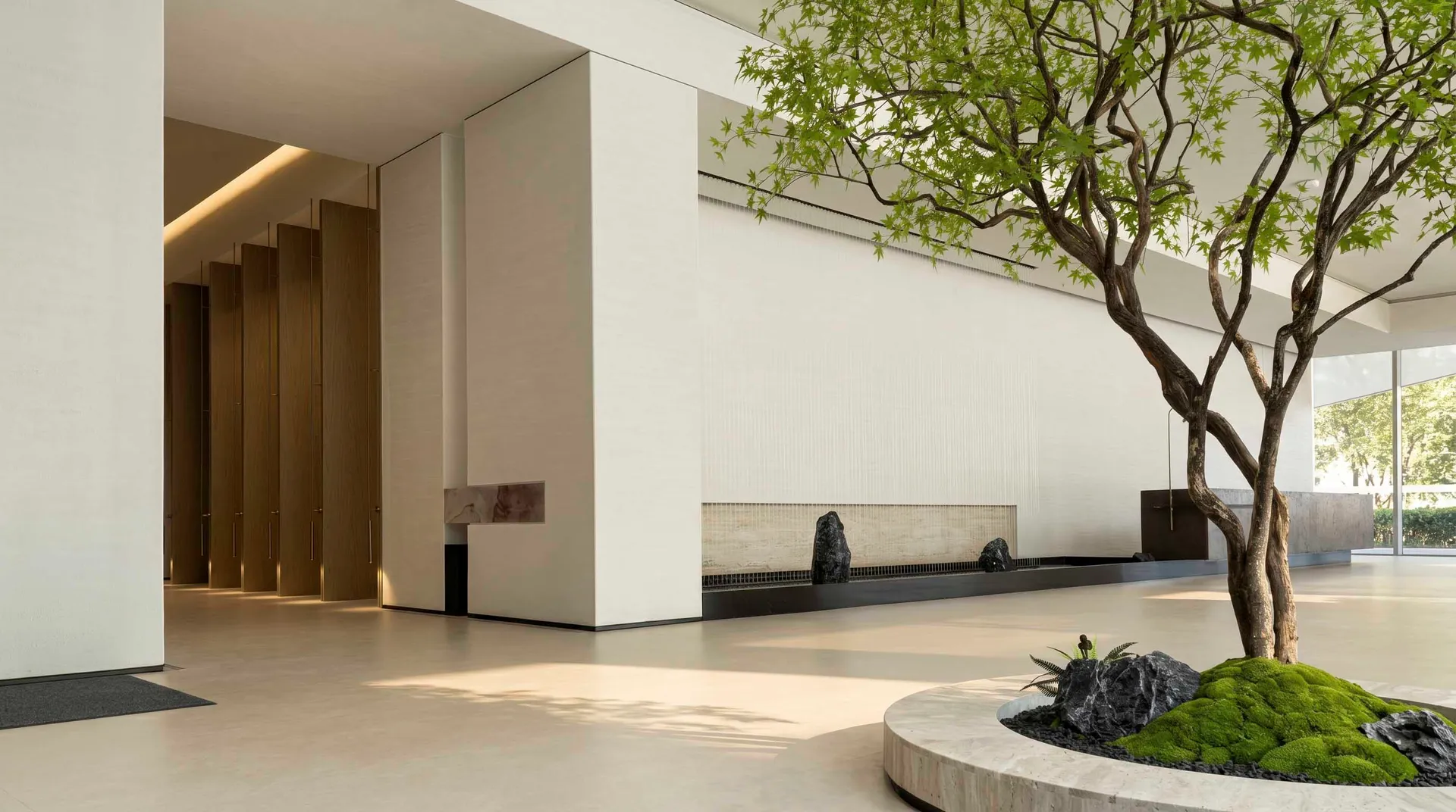 A modern building with a white exterior, featuring a large fireplace, a tree in the courtyard, and a stone wall, blending indoor and outdoor spaces with bright lighting