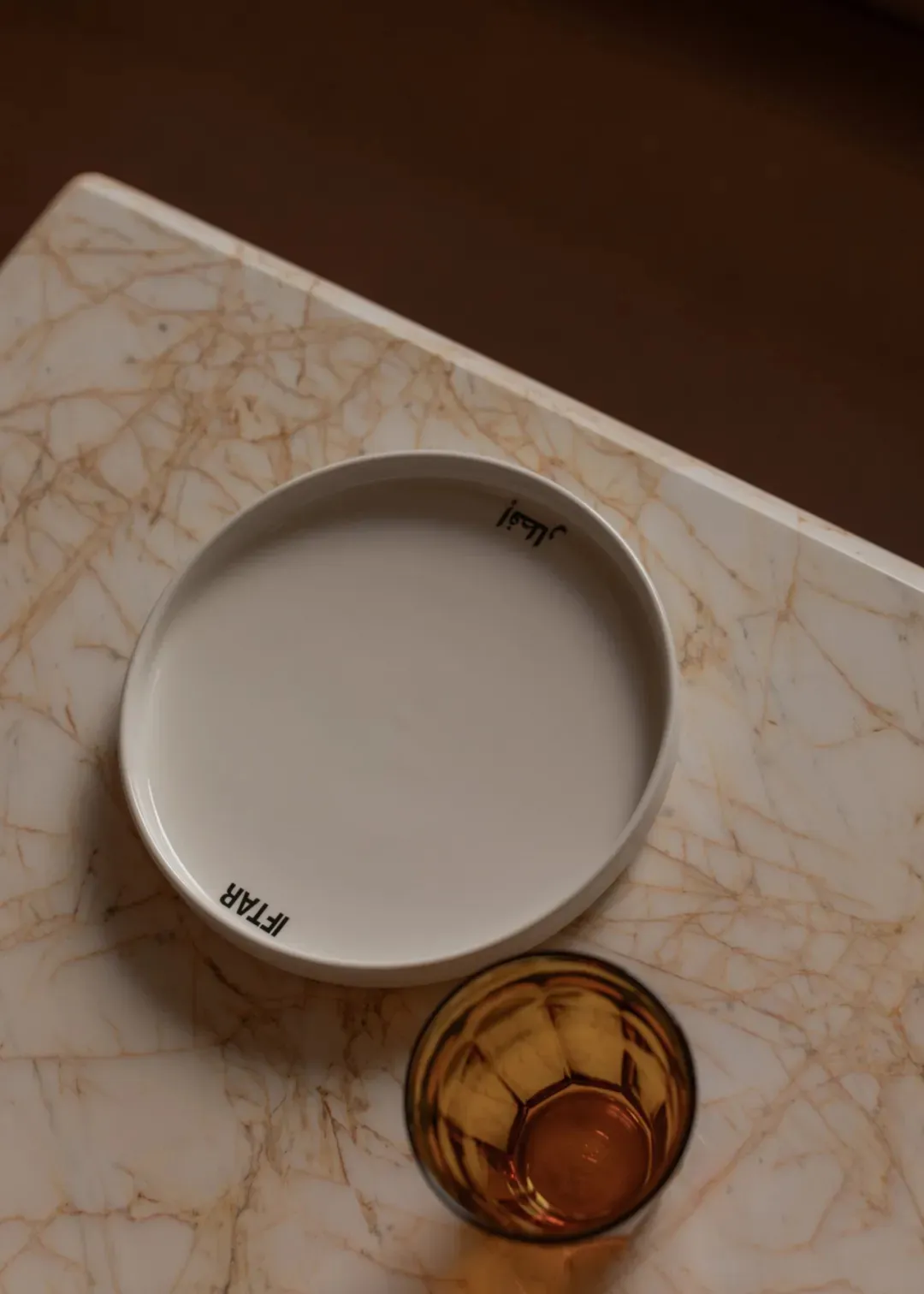 A white plate sits on a marble table in a dining room setting, creating a clean and elegant atmosphere