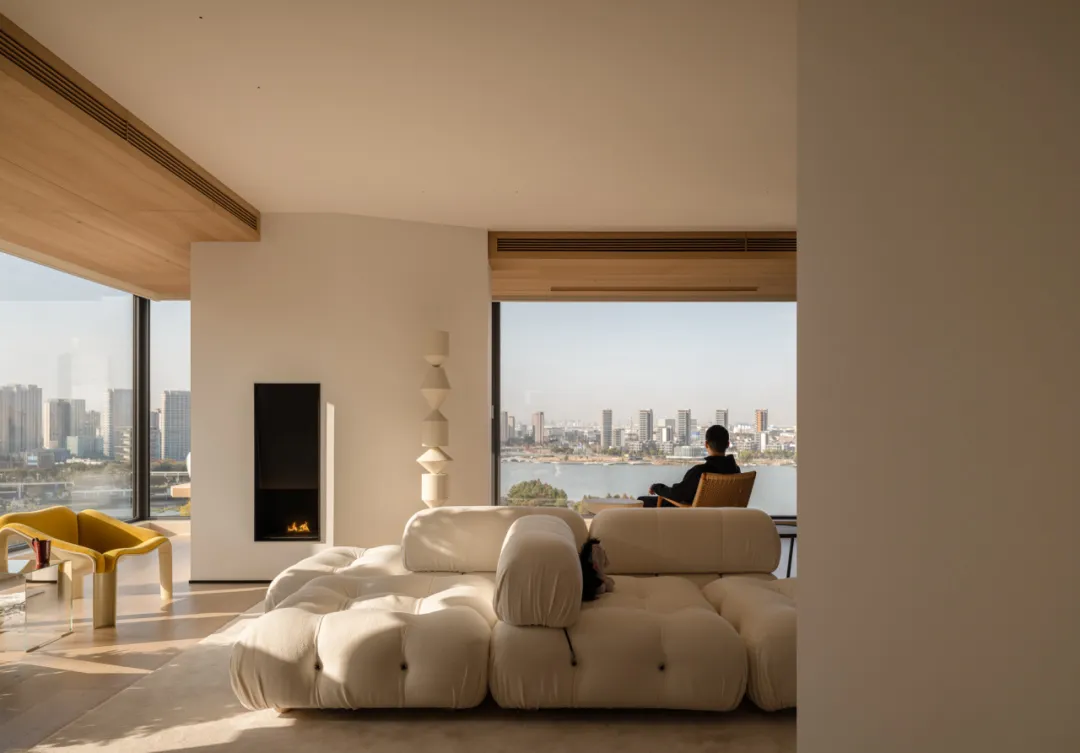 A modern living room with a white couch, a chair, and a fireplace, featuring clean lines and minimalistic design elements, with natural light streaming in through the windows