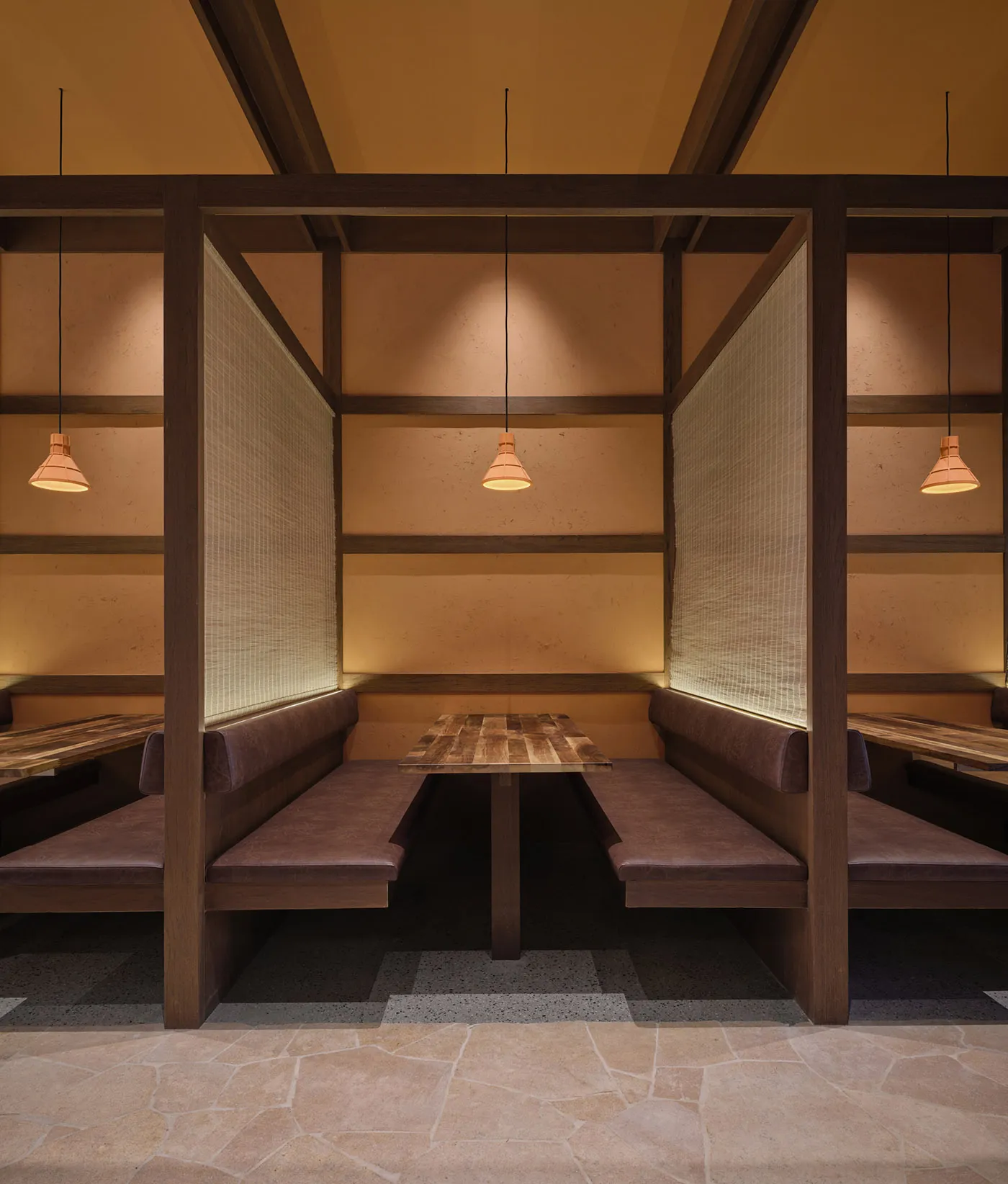 A modern restaurant with a wooden interior, featuring a dining area with tables and benches, a bar with a counter, and dim lighting creating a cozy ambiance