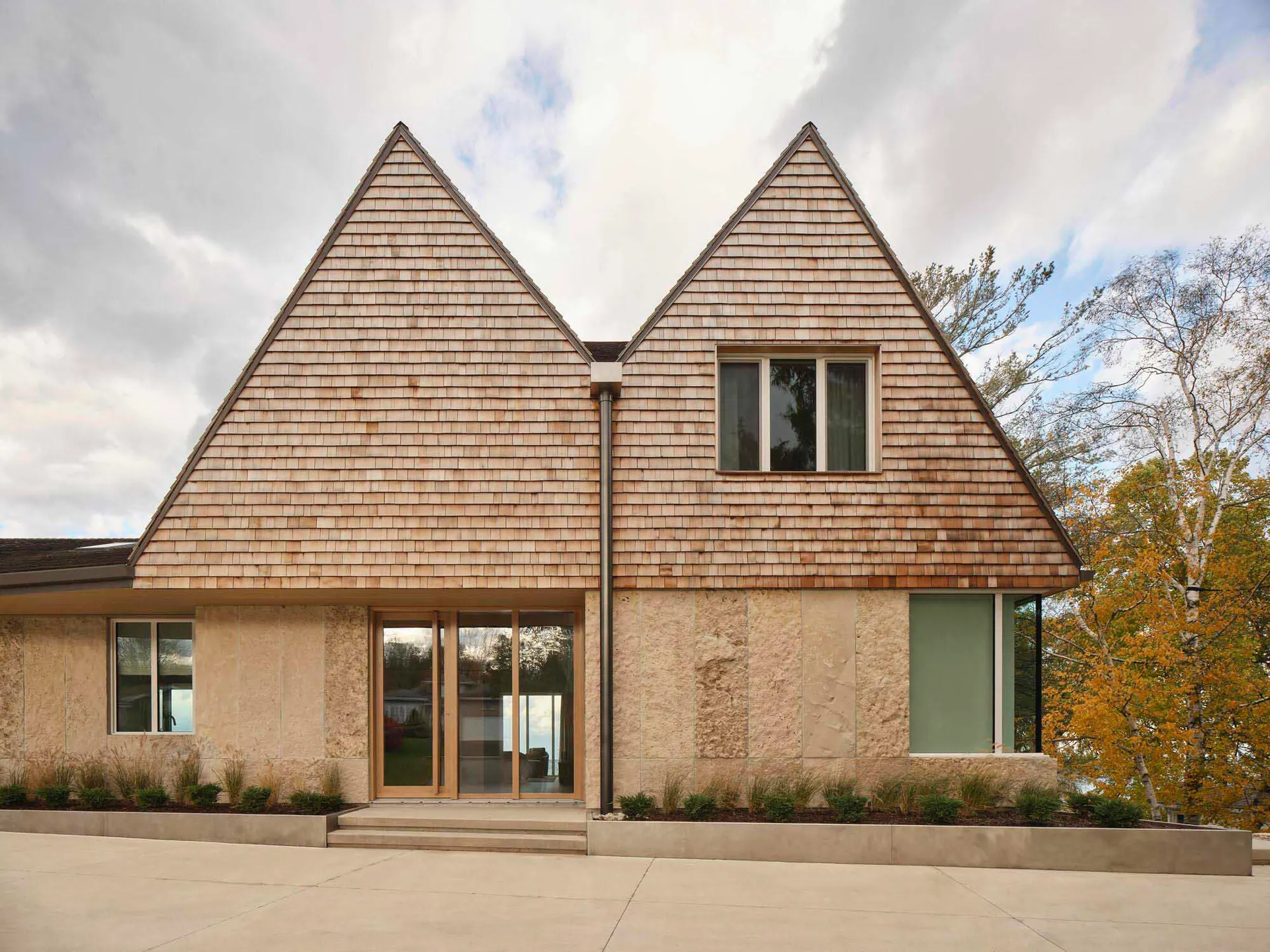 A warm and inviting beach house with a triangular shape, featuring a combination of stone and wood materials, and numerous windows for natural light