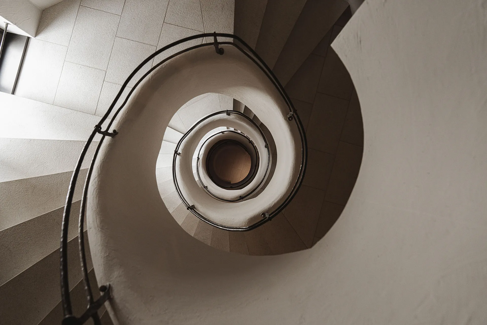 A dimly lit photograph of a historic spiral staircase with stone steps, part of a larger building, conveying a sense of architectural beauty and historical significance