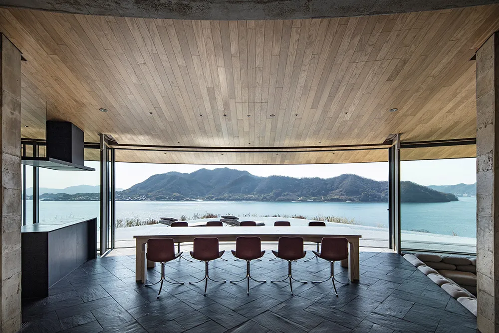 A large dining room with a wooden floor, a dining table, and chairs, offering a cozy and inviting atmosphere with a view of the water outside