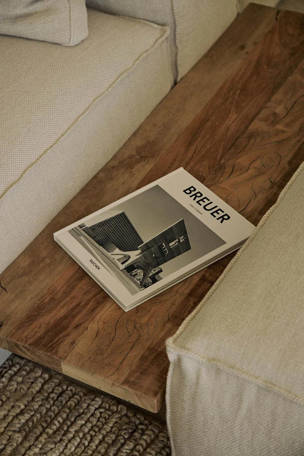 A modern hotel lobby with a white couch on a wooden floor, a magazine on top, and a sleek building in the background