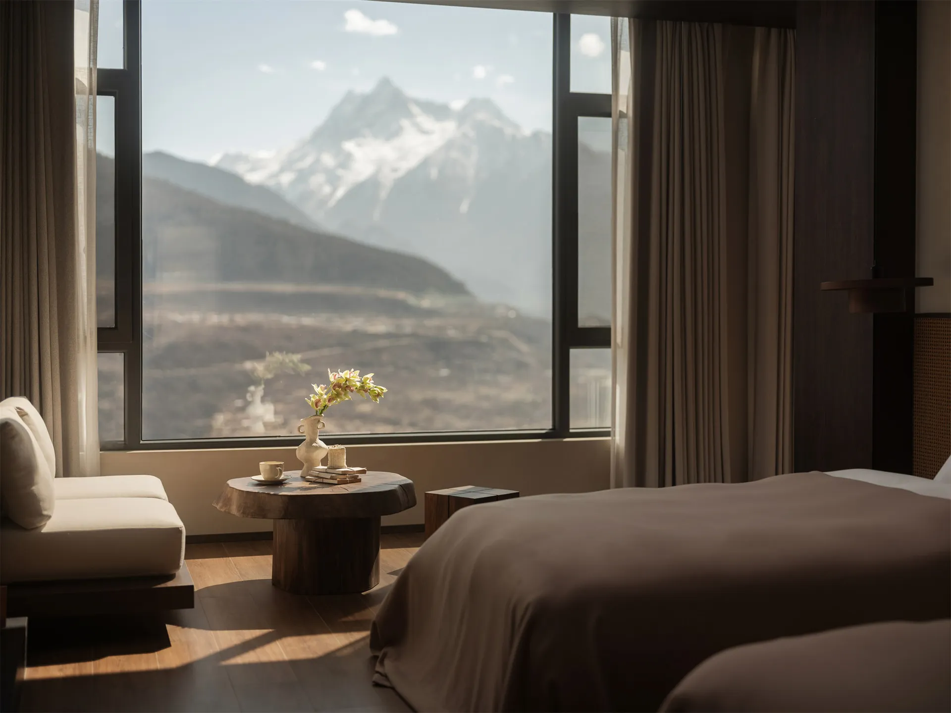A bedroom with a large window offering a view of the mountains, featuring a bed, chair, and table in a cozy and inviting atmosphere with natural light