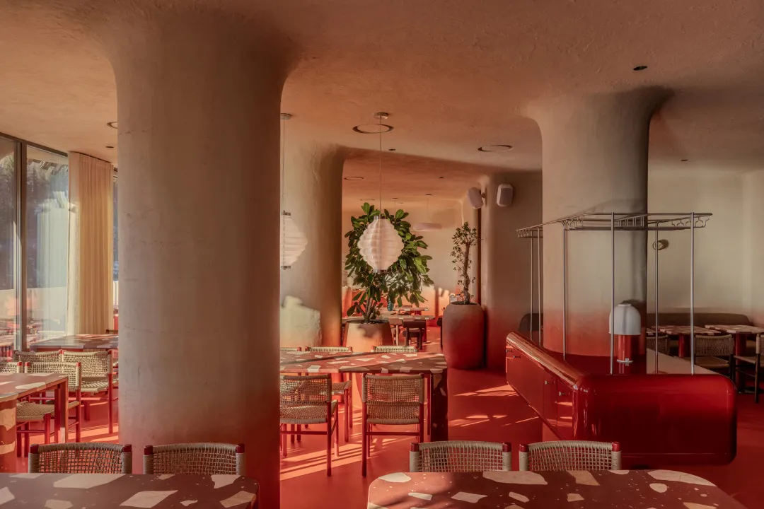 Cozy modern restaurant interior with red walls, wooden furniture, and potted plants, featuring soft warm lighting