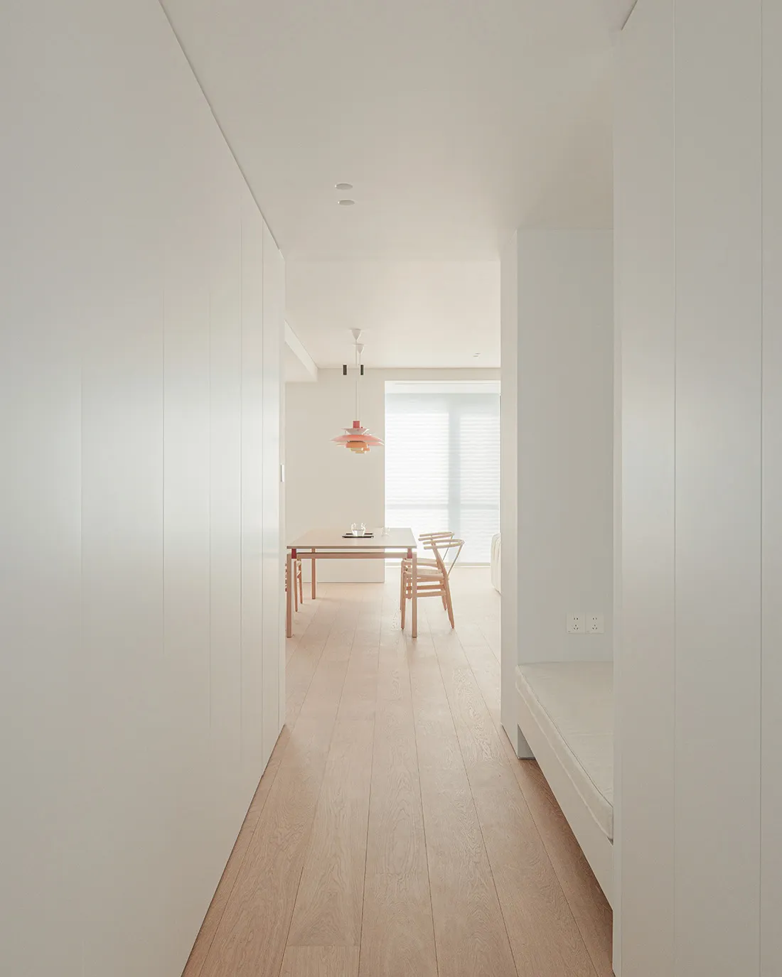 A bright and welcoming room with a wooden floor, a bed on the right, a dining table and chair in the center, and white walls