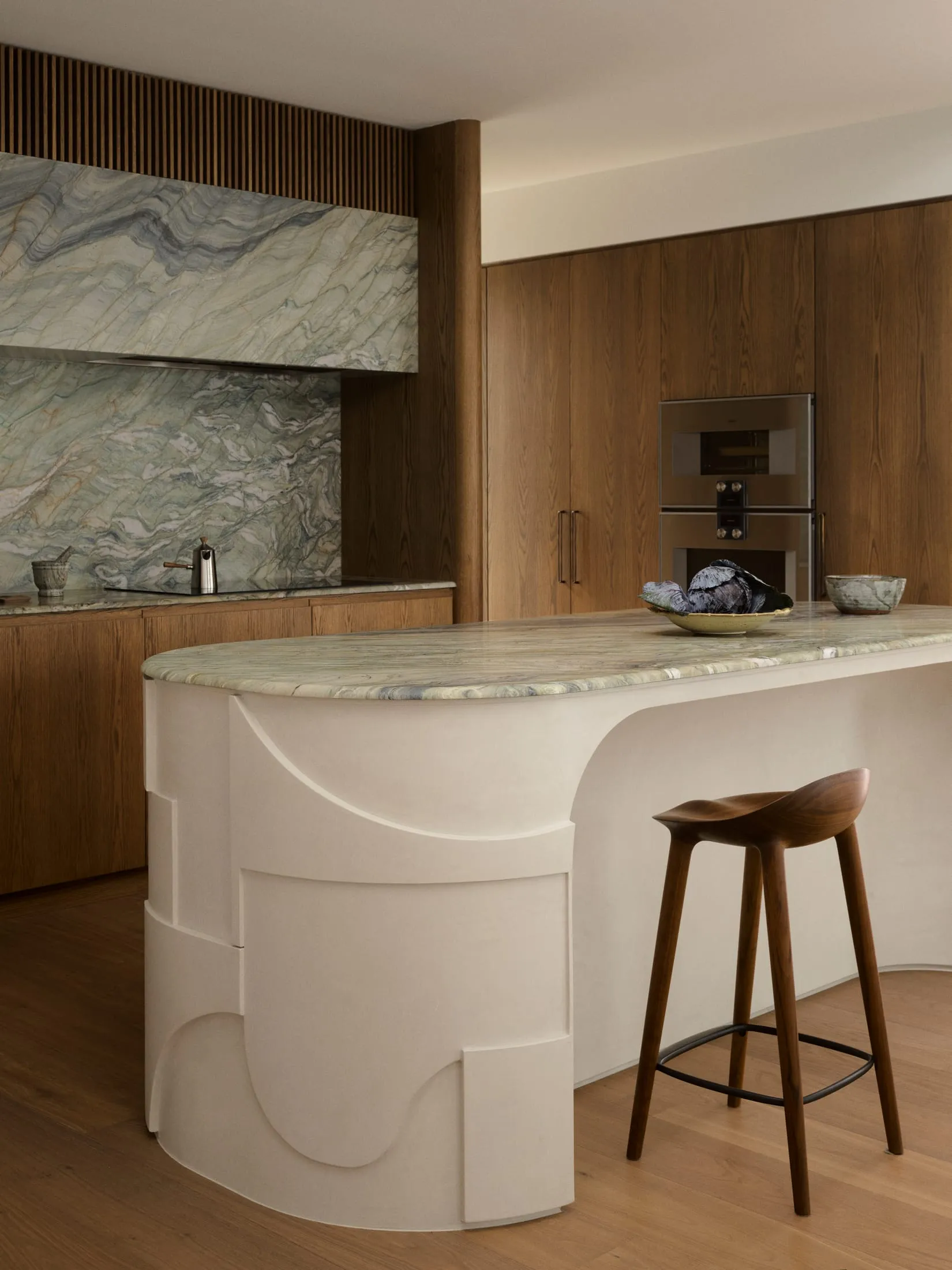 Modern kitchen with a white marble countertop, brown wooden cabinets, a sink, refrigerator, and microwave, with a chair and a bowl on the countertop