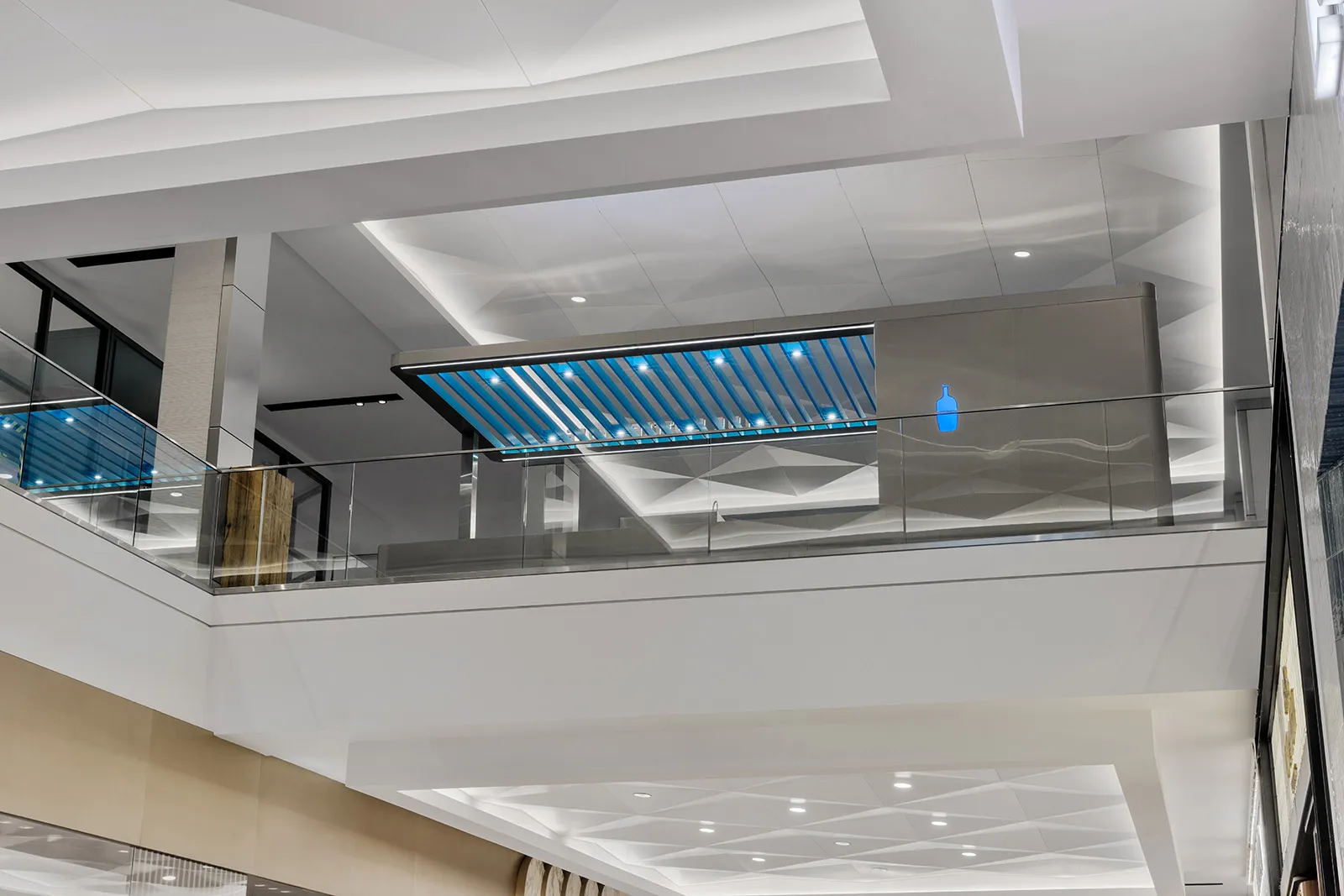 Large, open lobby with a blue and white color scheme, a glass ceiling, and a prominent blue bar, creating a welcoming and inviting atmosphere