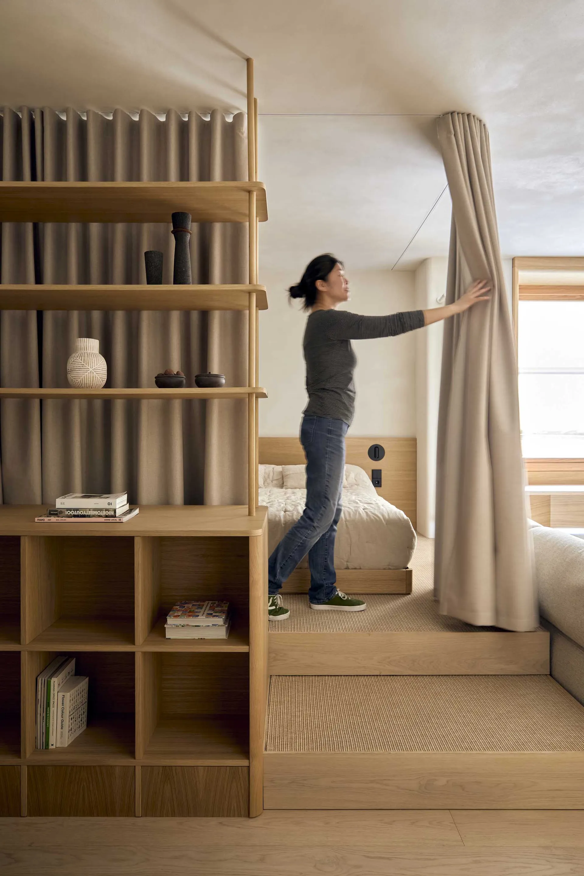 A well-lit bedroom with a bed in the center, a bookshelf on the left, and a window on the right, creating a comfortable atmosphere