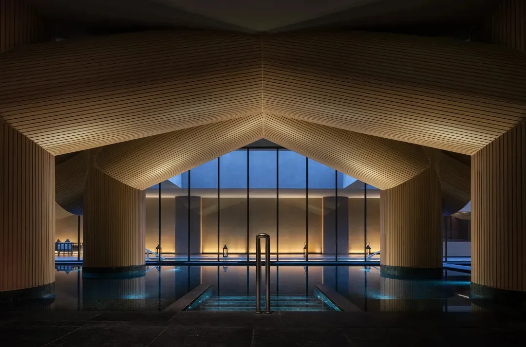 A relaxing pool area with a wooden ceiling, surrounded by a wooden deck and potted plants, with a calm atmosphere