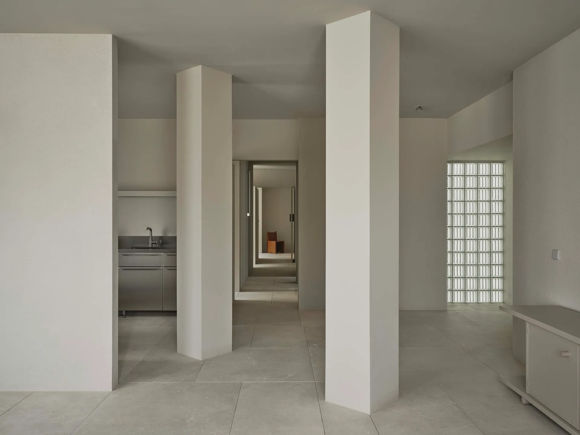 A bright and inviting kitchen and hallway with white walls, tile floors, and natural light from windows