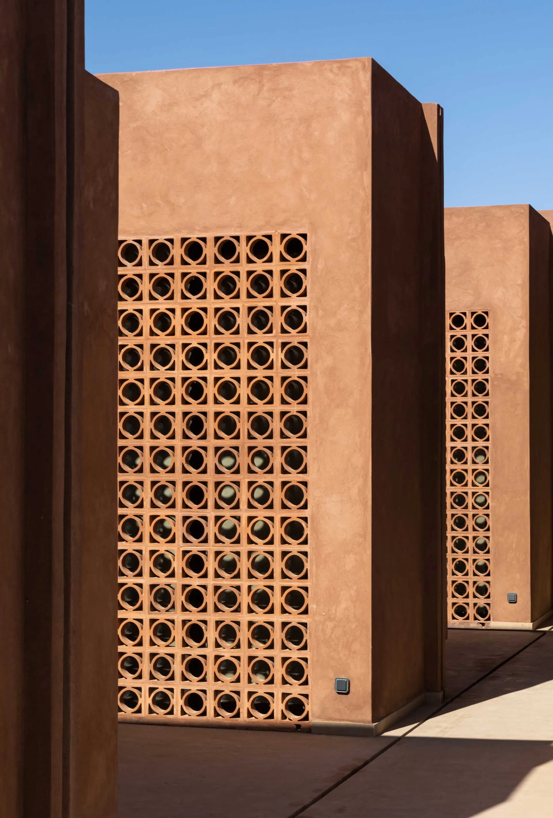 Photograph of a brown brick building with a unique patterned wall and small windows, taken during the daytime with natural light