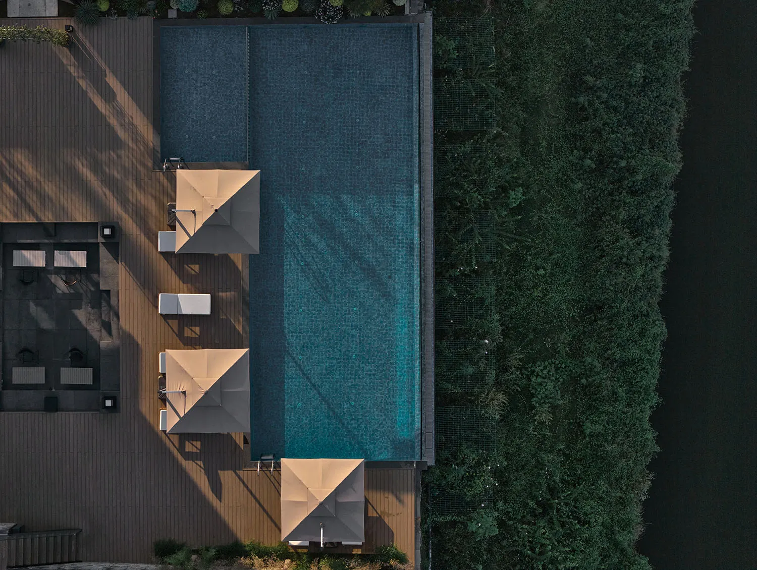 A well-maintained pool area with a blue pool surrounded by umbrellas in a backyard setting