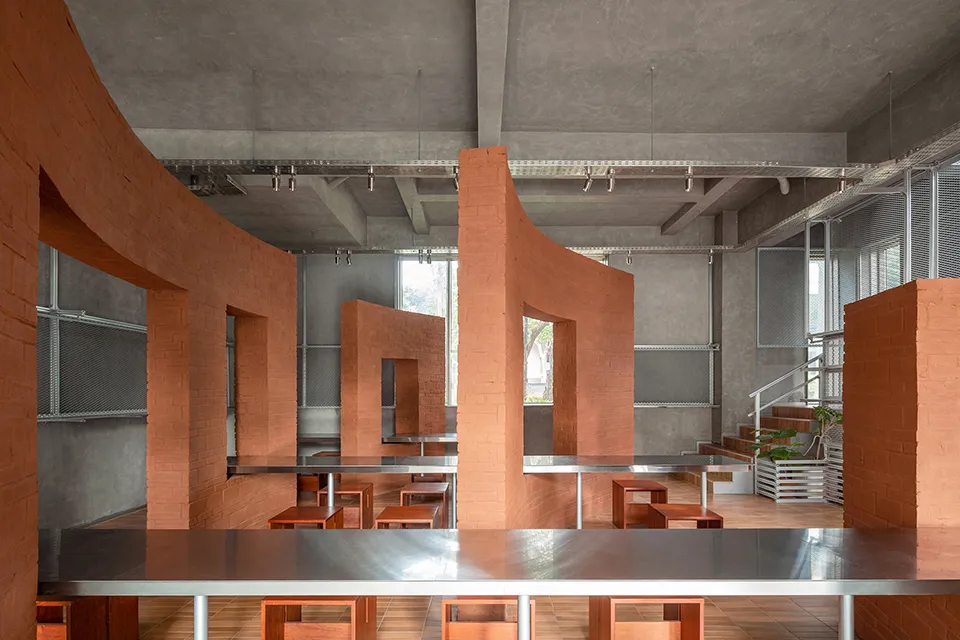 A modern restaurant with a large dining table and benches, surrounded by concrete walls and wooden accents, in a well-lit space
