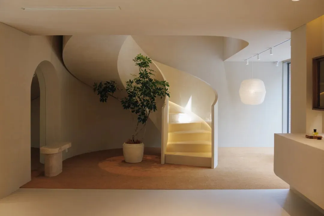 A modern white staircase in a bright and airy room with a potted plant and a white floor and wall