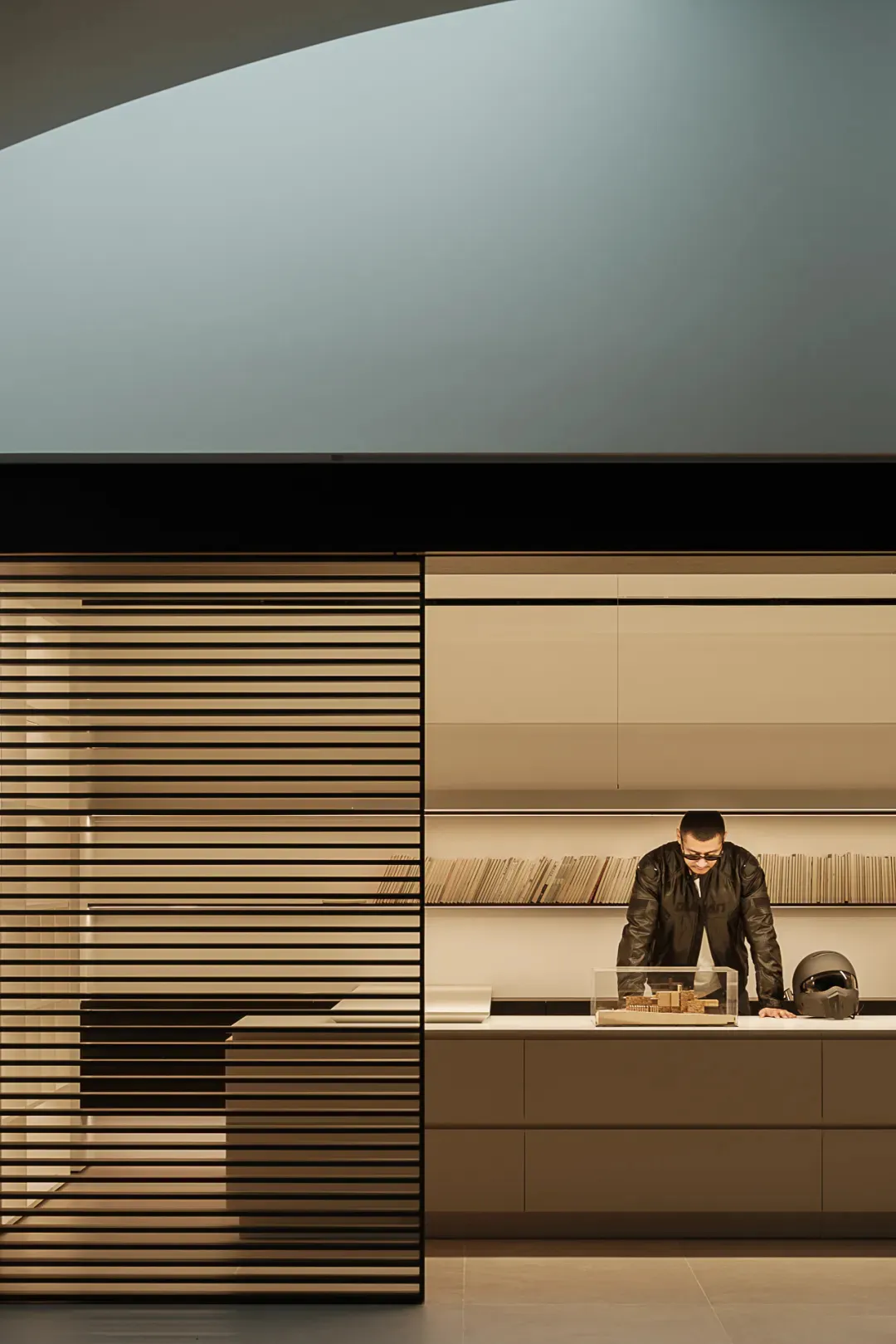 A dimly lit modern room with a wooden counter, a laptop, and a man working, creating a cozy atmosphere