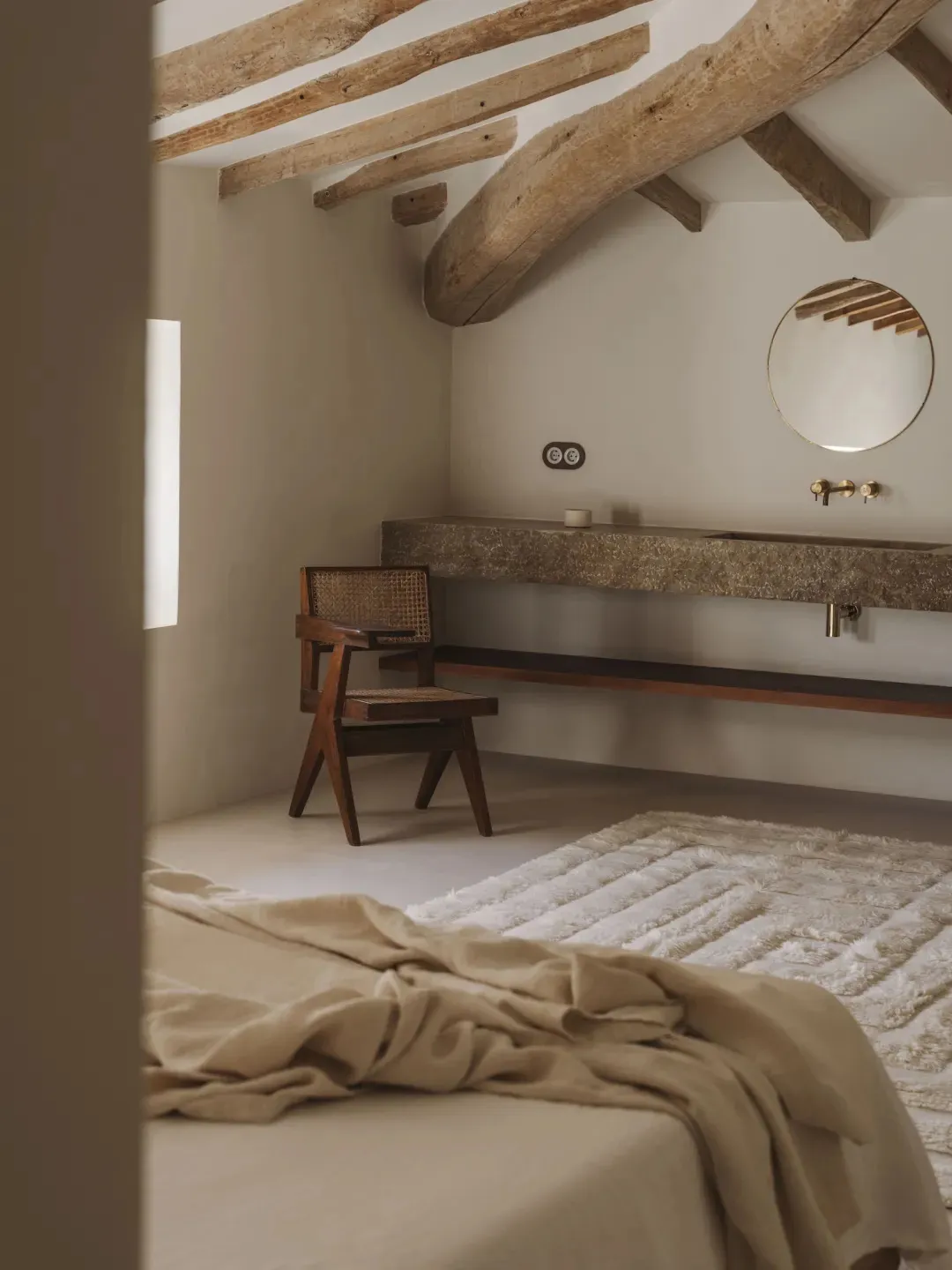 Cozy bedroom with a wooden bed, chair, and sink, featuring a white blanket and wooden walls