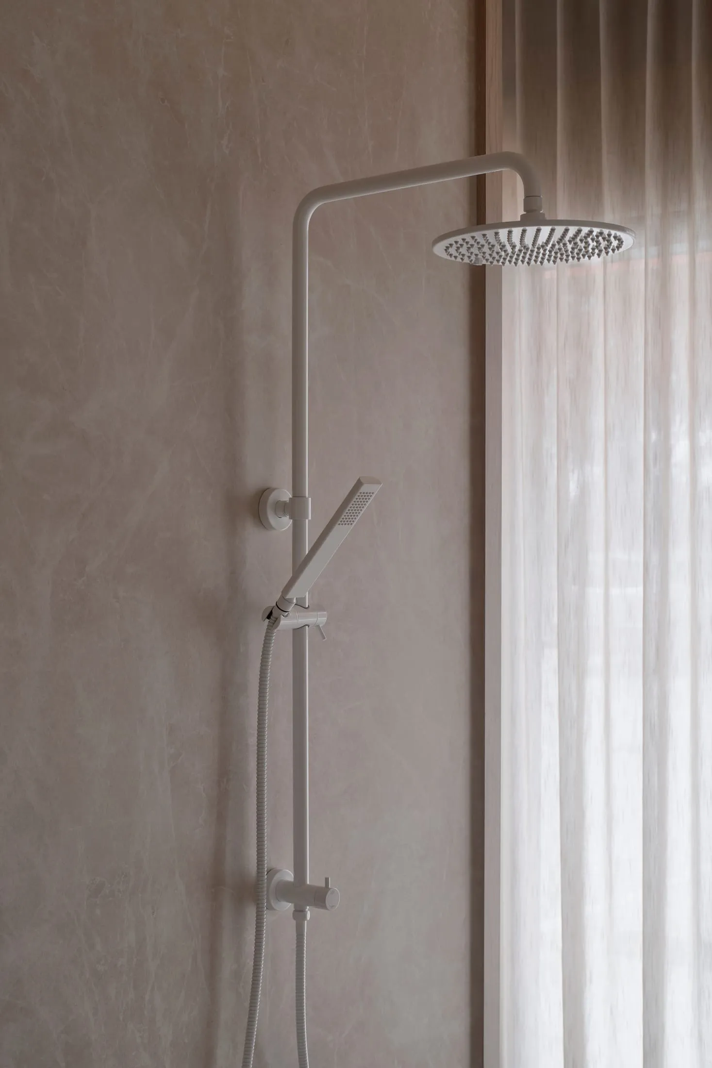 Bathroom with a white shower head on a concrete wall, natural light from a window, and a minimalist aesthetic