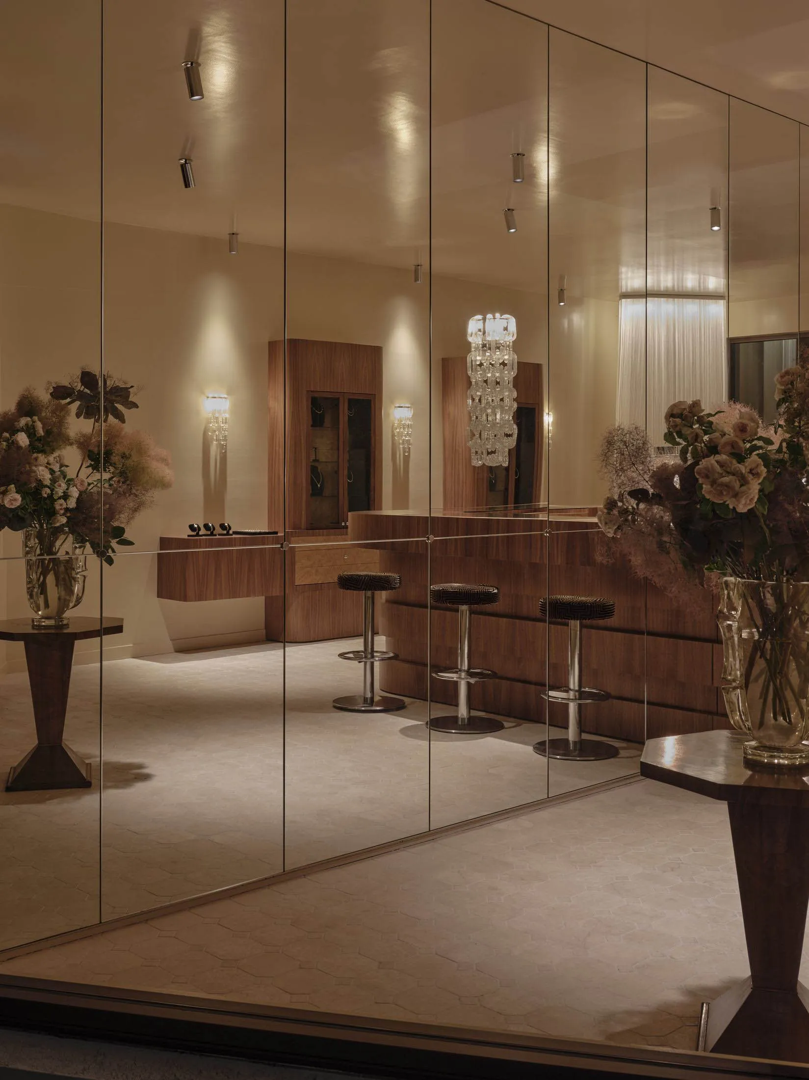 A well-lit modern room with a mirror, bar, chairs, dining table, vases, and potted plants, creating a comfortable and inviting atmosphere