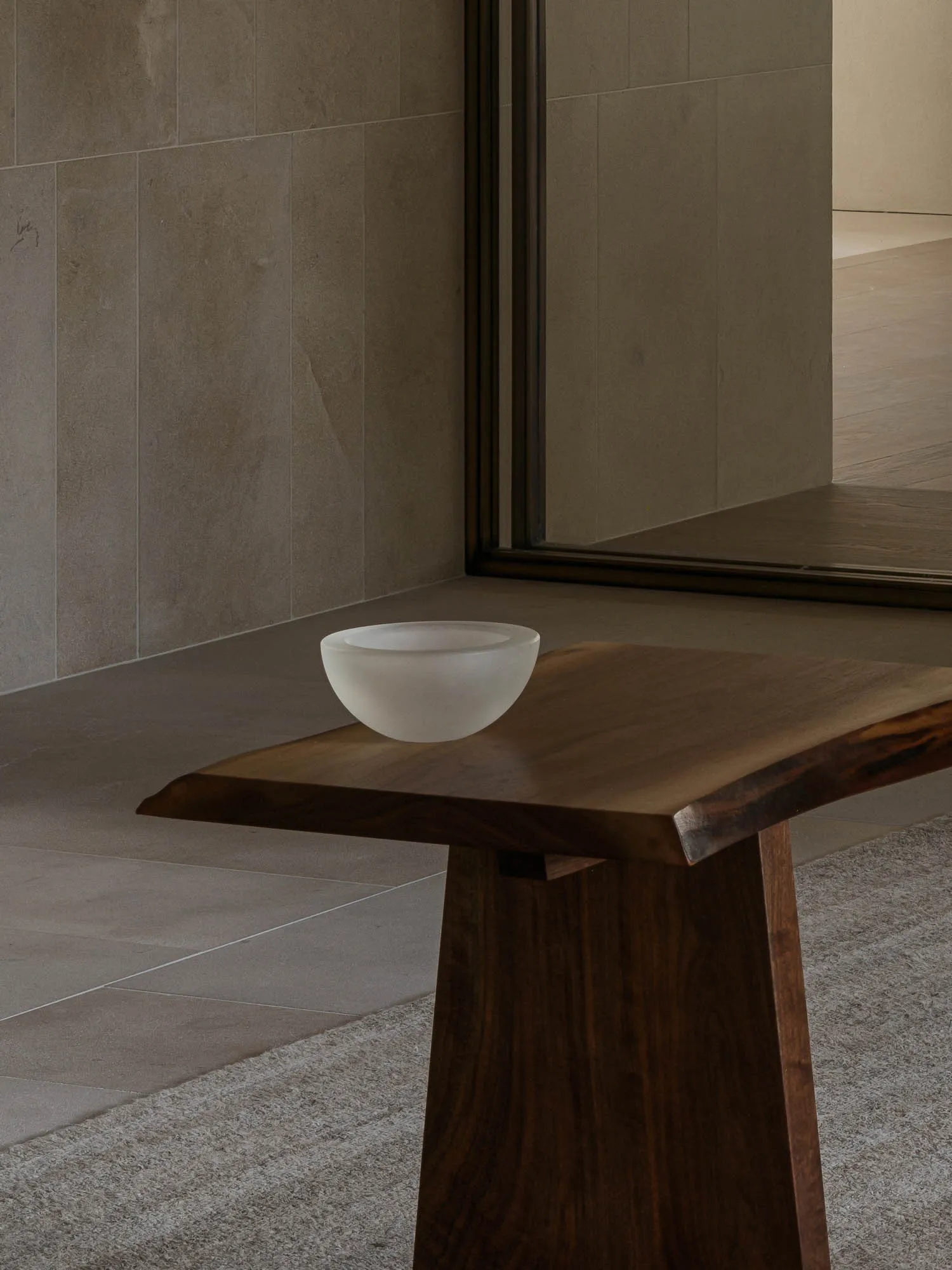 A well-lit bathroom with a wooden table and a white bowl, featuring a shower in the background