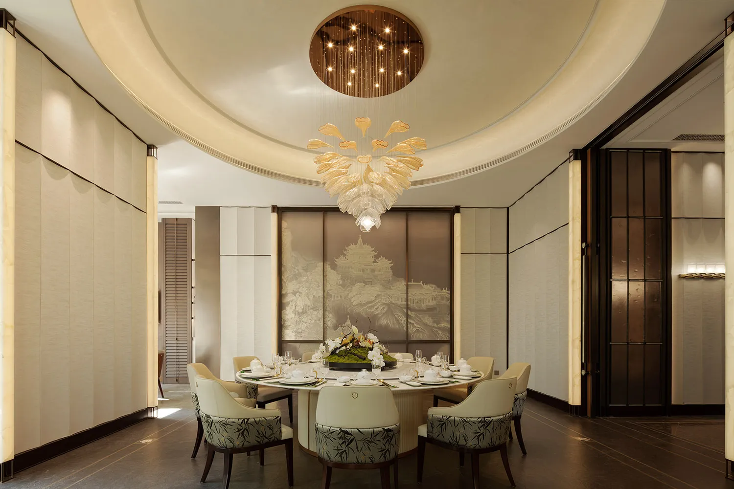 Dining room with a round table and chairs, set with dishes and decorations, surrounded by artwork and a large chandelier, in a modern and sophisticated style