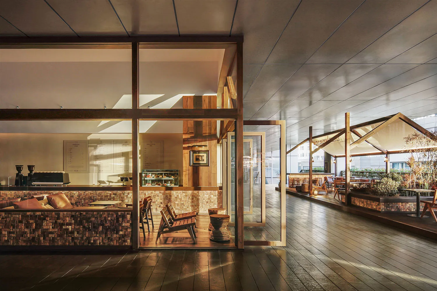 A modern restaurant interior with a wooden floor, dining tables, and chairs, featuring a large window and soft warm lighting