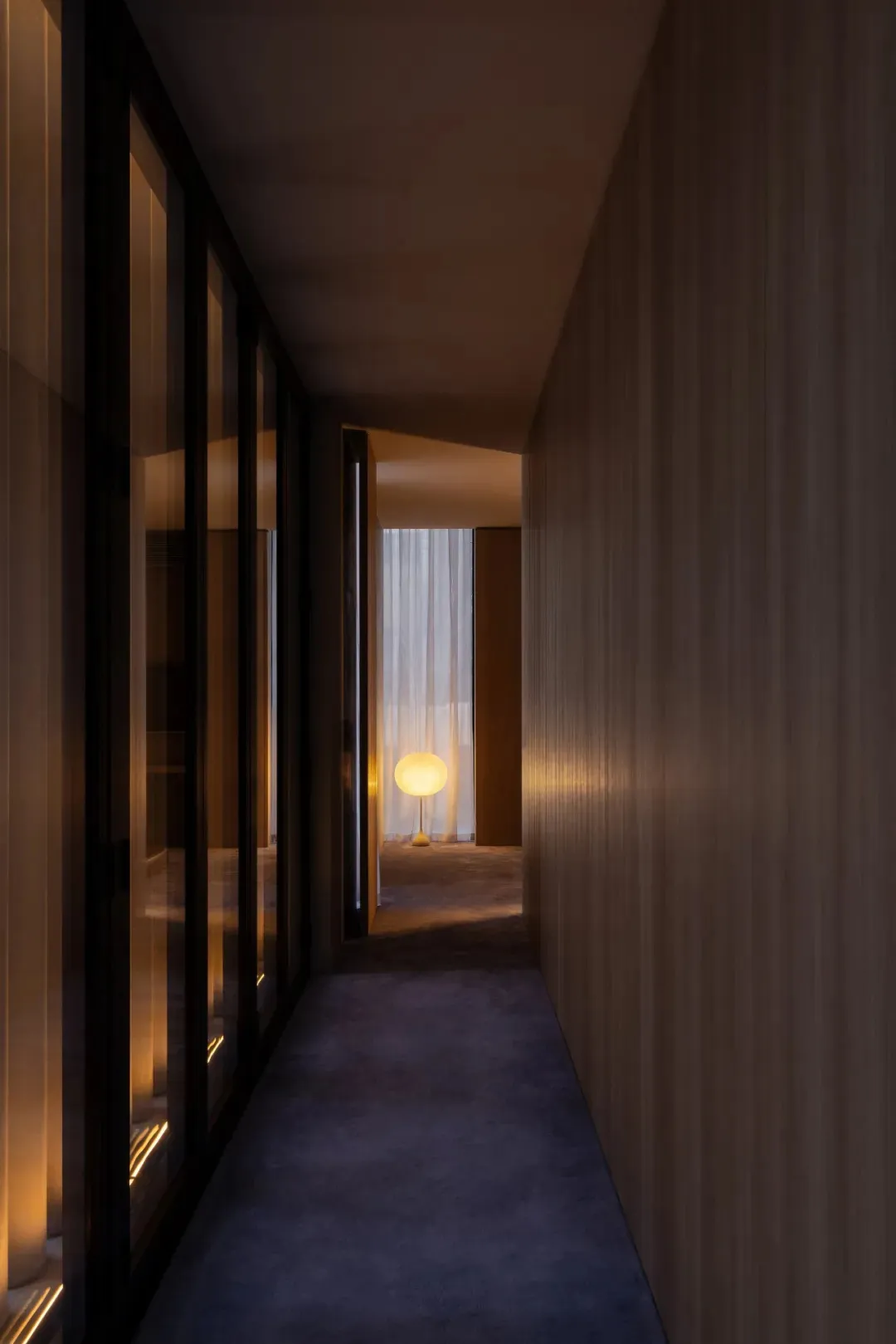 Narrow hallway with wooden floor and walls, dim lighting, and a bed on the left, creating a cozy and intimate atmosphere