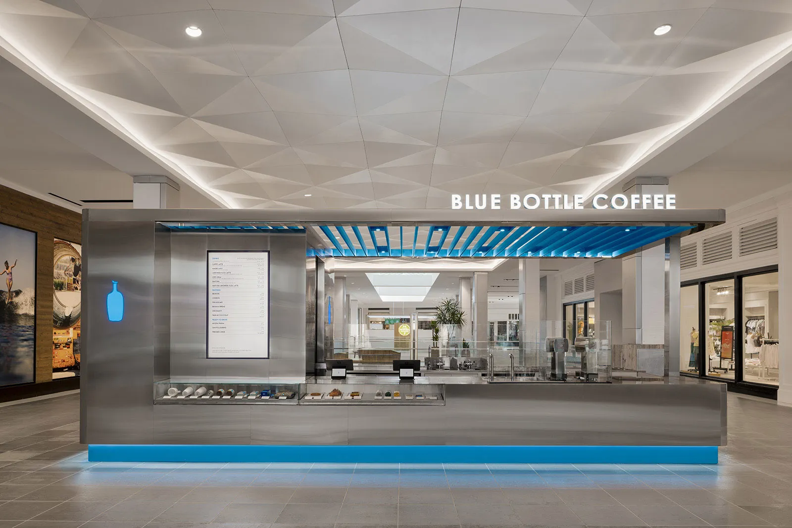A modern coffee shop with a blue and white color scheme, featuring a variety of seating options, potted plants, and a welcoming atmosphere