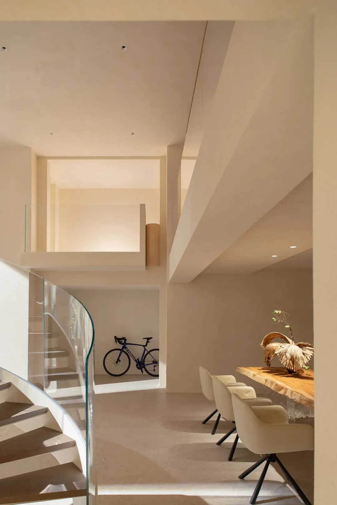 Modern living room with a glass staircase, dining table, and wooden furniture, well-lit with natural light