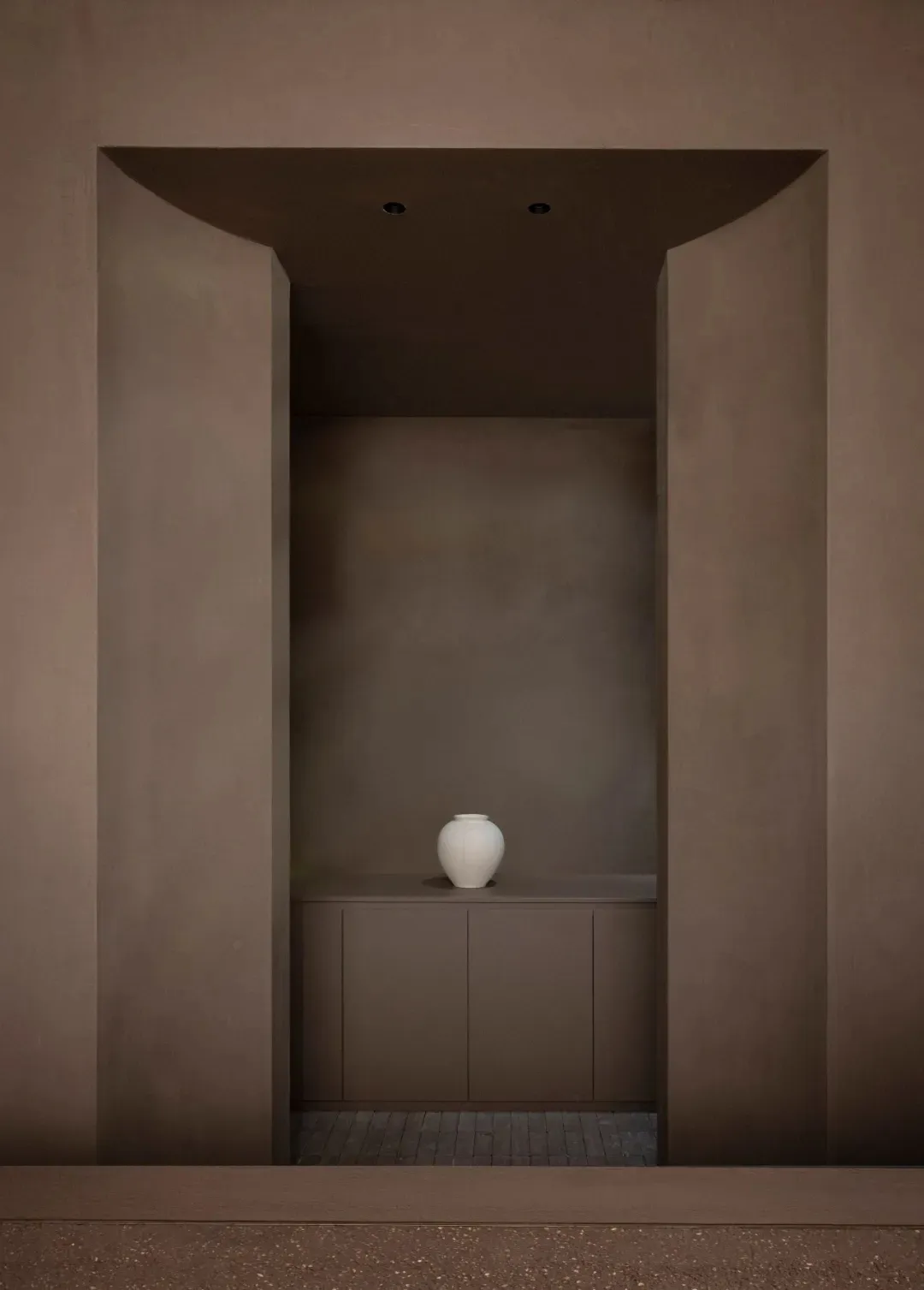A small, simple room with a brown color scheme and a white vase on a counter as the main point of interest